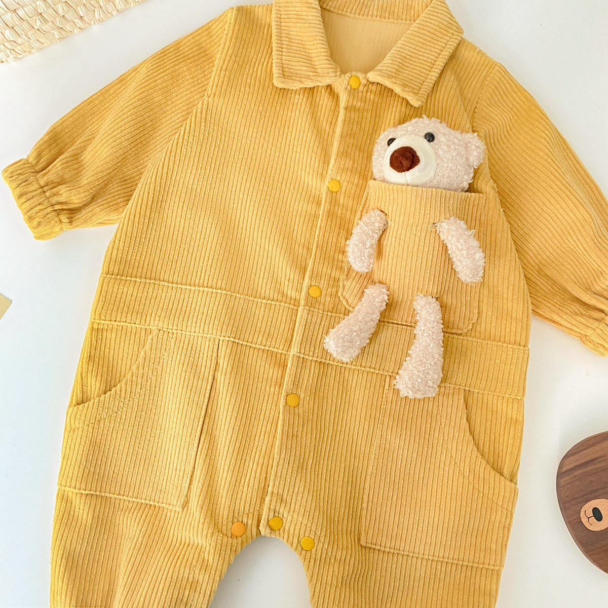 Baby romper featuring a 3D cartoon bear patch design, made from soft corduroy fabric with a button front closure, available in yellow and apricot.