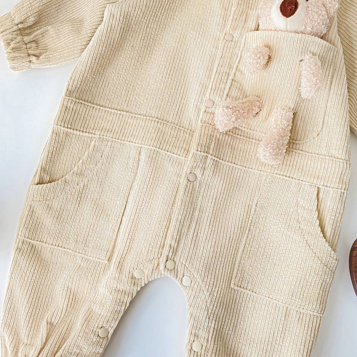 Baby romper featuring a 3D cartoon bear patch design, made from soft corduroy fabric with a button front closure, available in yellow and apricot.