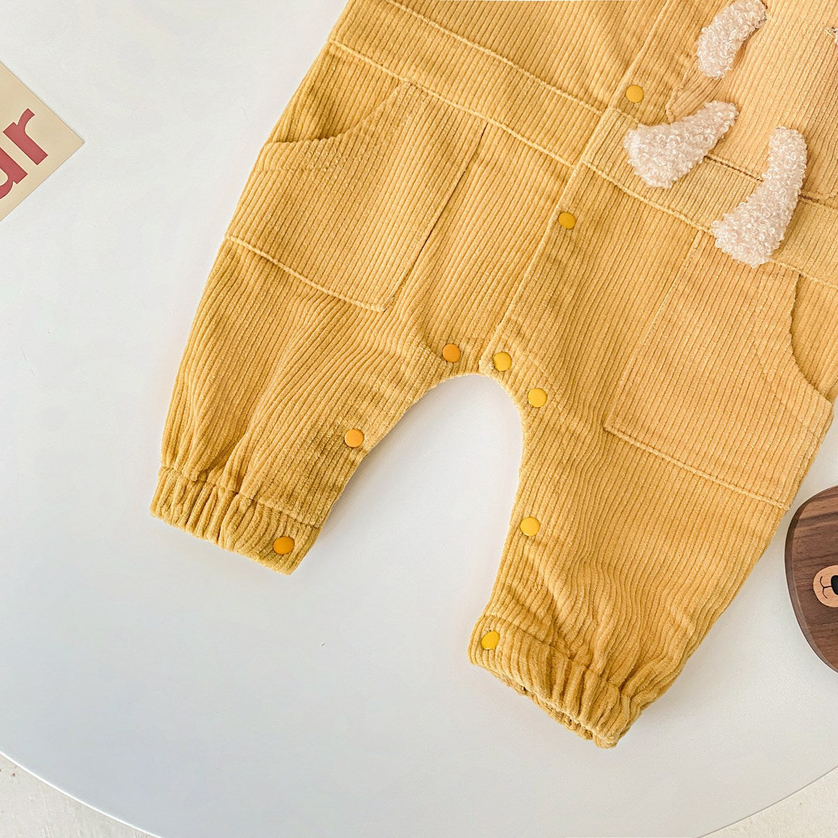 Baby romper featuring a 3D cartoon bear patch design, made from soft corduroy fabric with a button front closure, available in yellow and apricot.