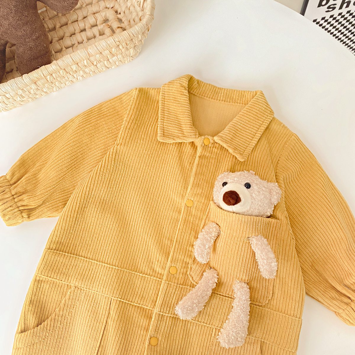 Baby romper featuring a 3D cartoon bear patch design, made from soft corduroy fabric with a button front closure, available in yellow and apricot.