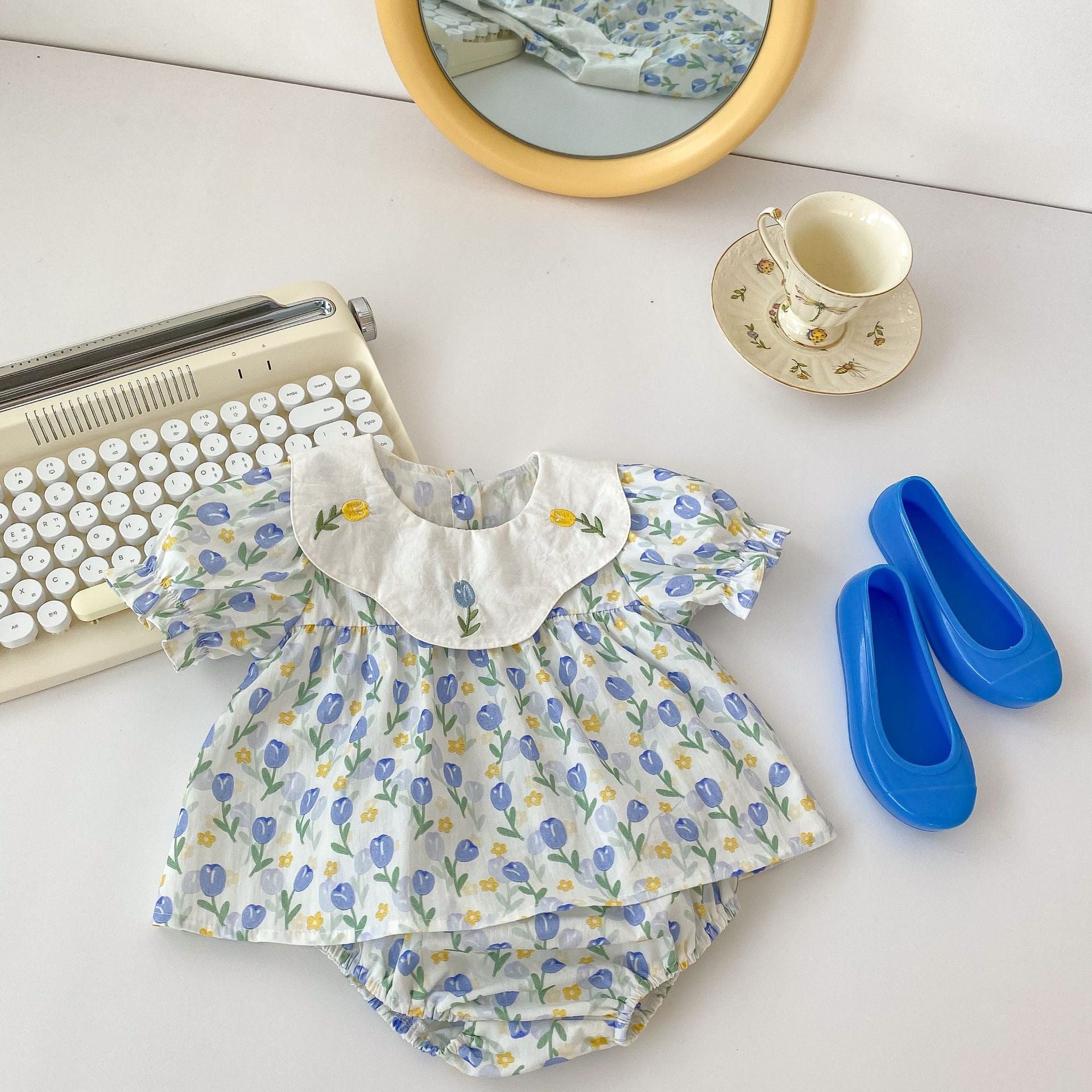 Baby girl wearing a blue floral embroidered crewneck top with doll neck design, showcasing delicate flower patterns.