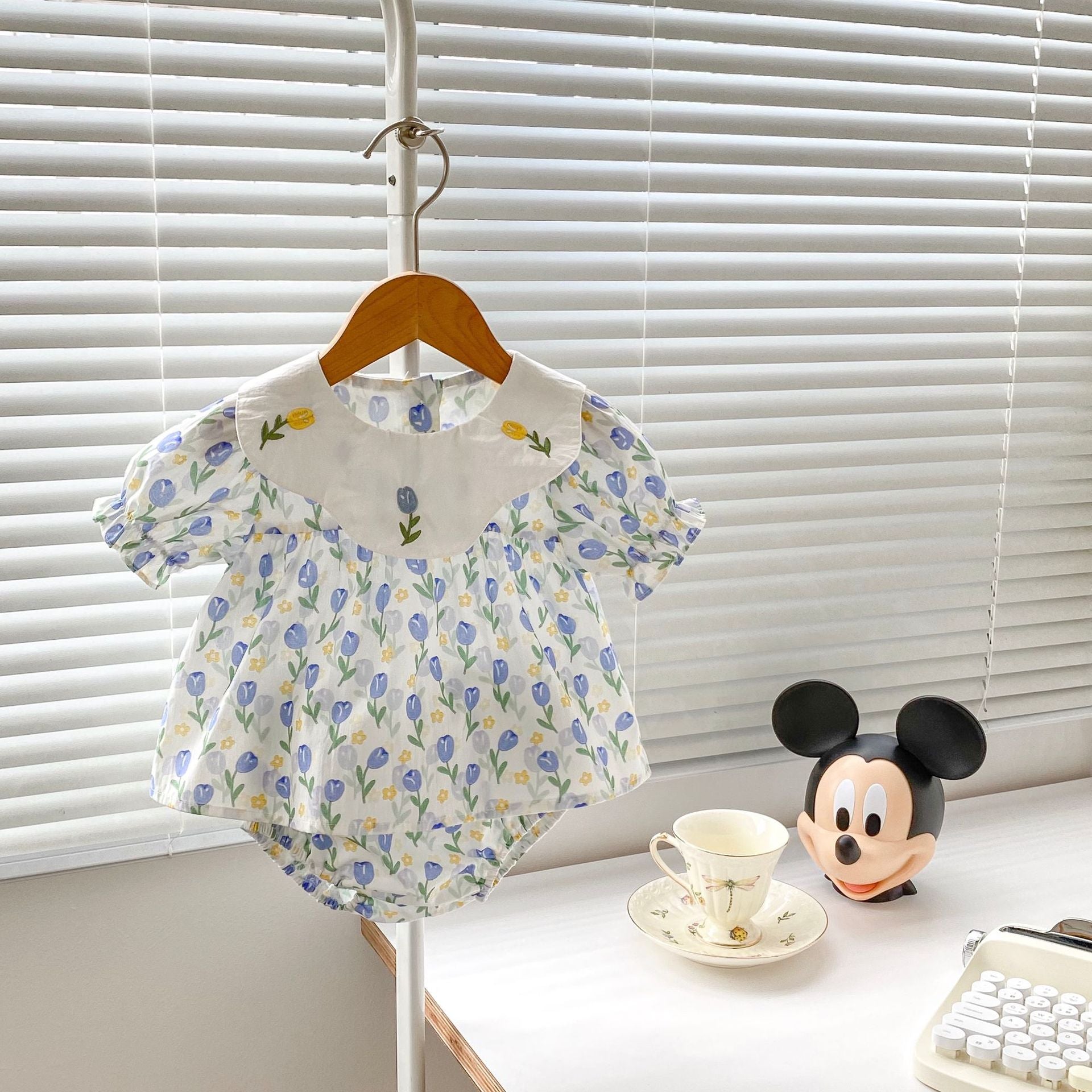 Baby girl wearing a blue floral embroidered crewneck top with doll neck design, showcasing delicate flower patterns.