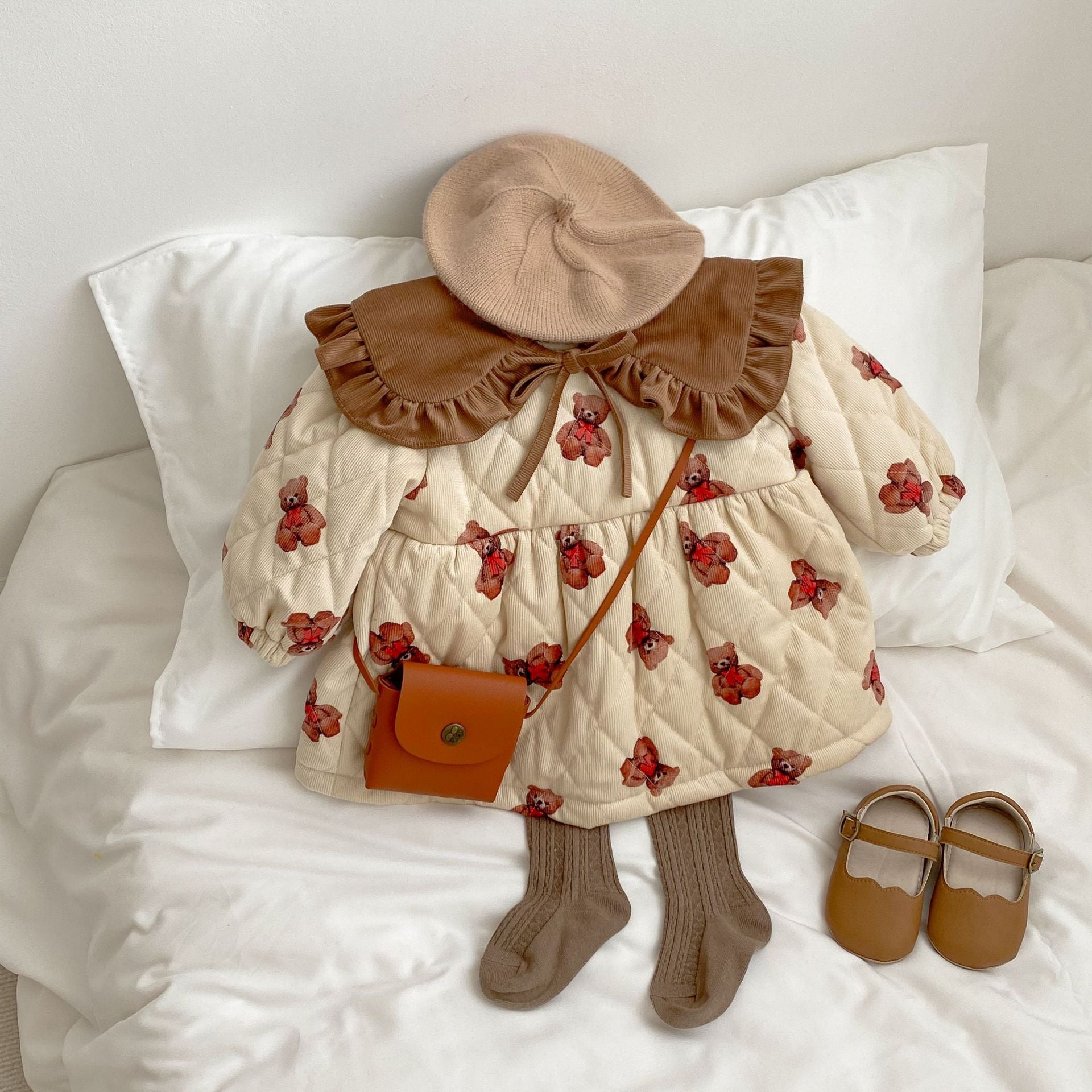 A cozy quilted baby dress featuring a cute cartoon bear graphic, available in brown and coffee colors.