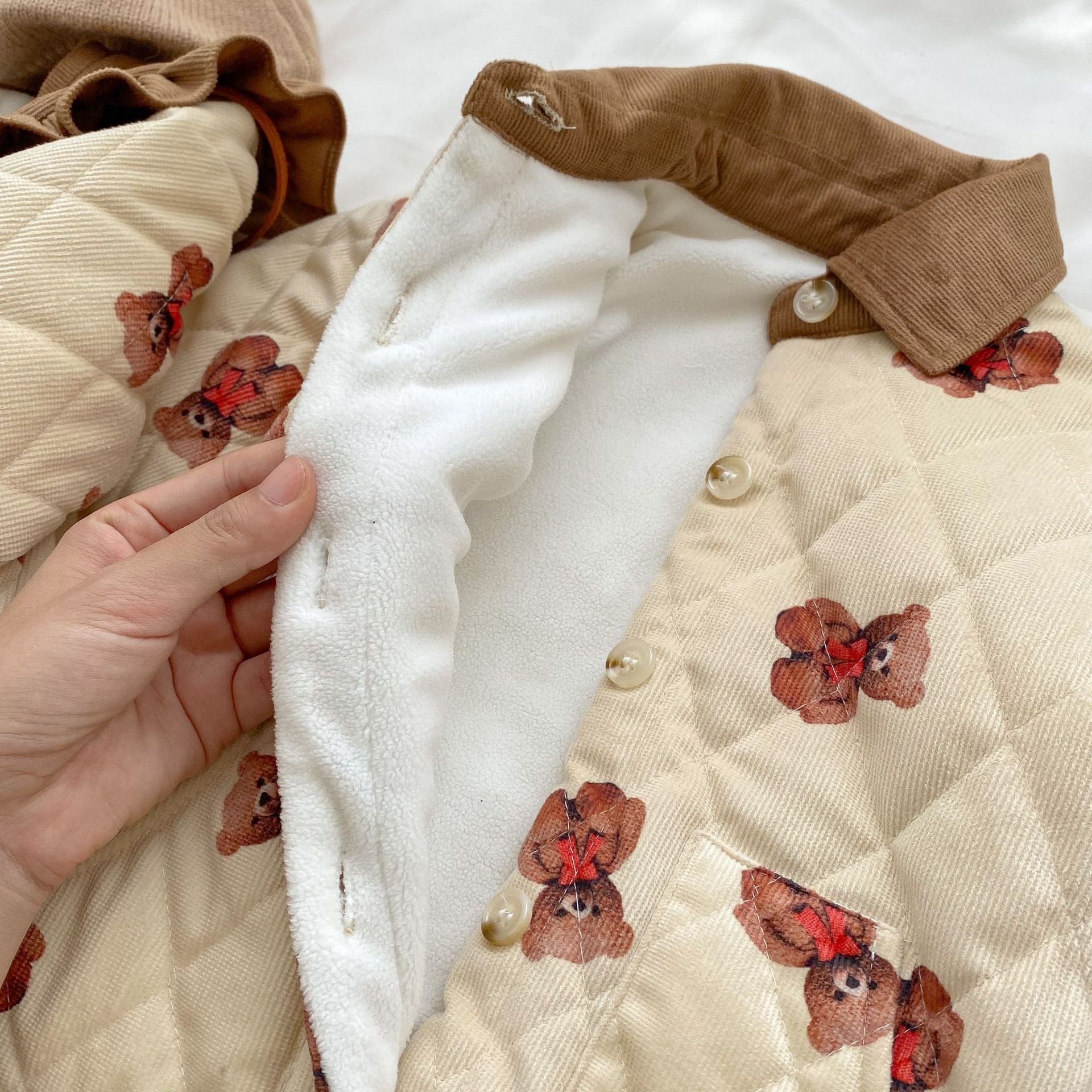 A cozy quilted baby dress featuring a cute cartoon bear graphic, available in brown and coffee colors.