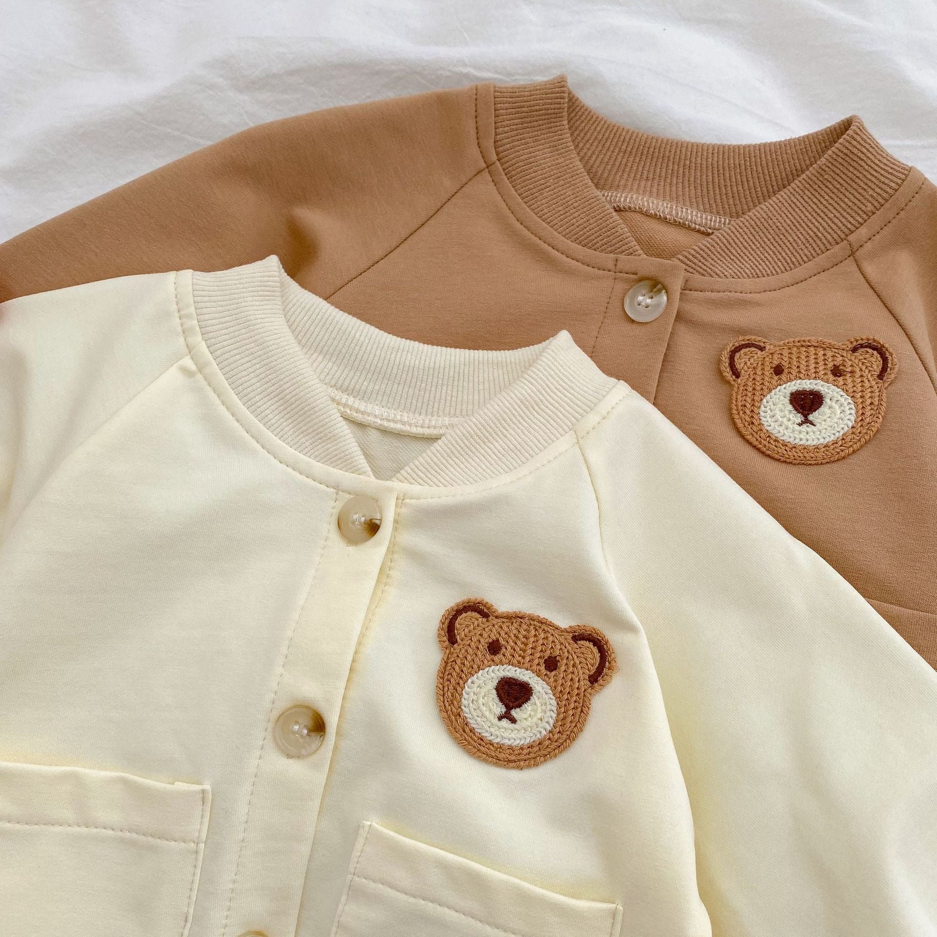 A cute baby wearing a cartoon bear patched romper and coat set in beige, showcasing its adorable design and premium cotton material.