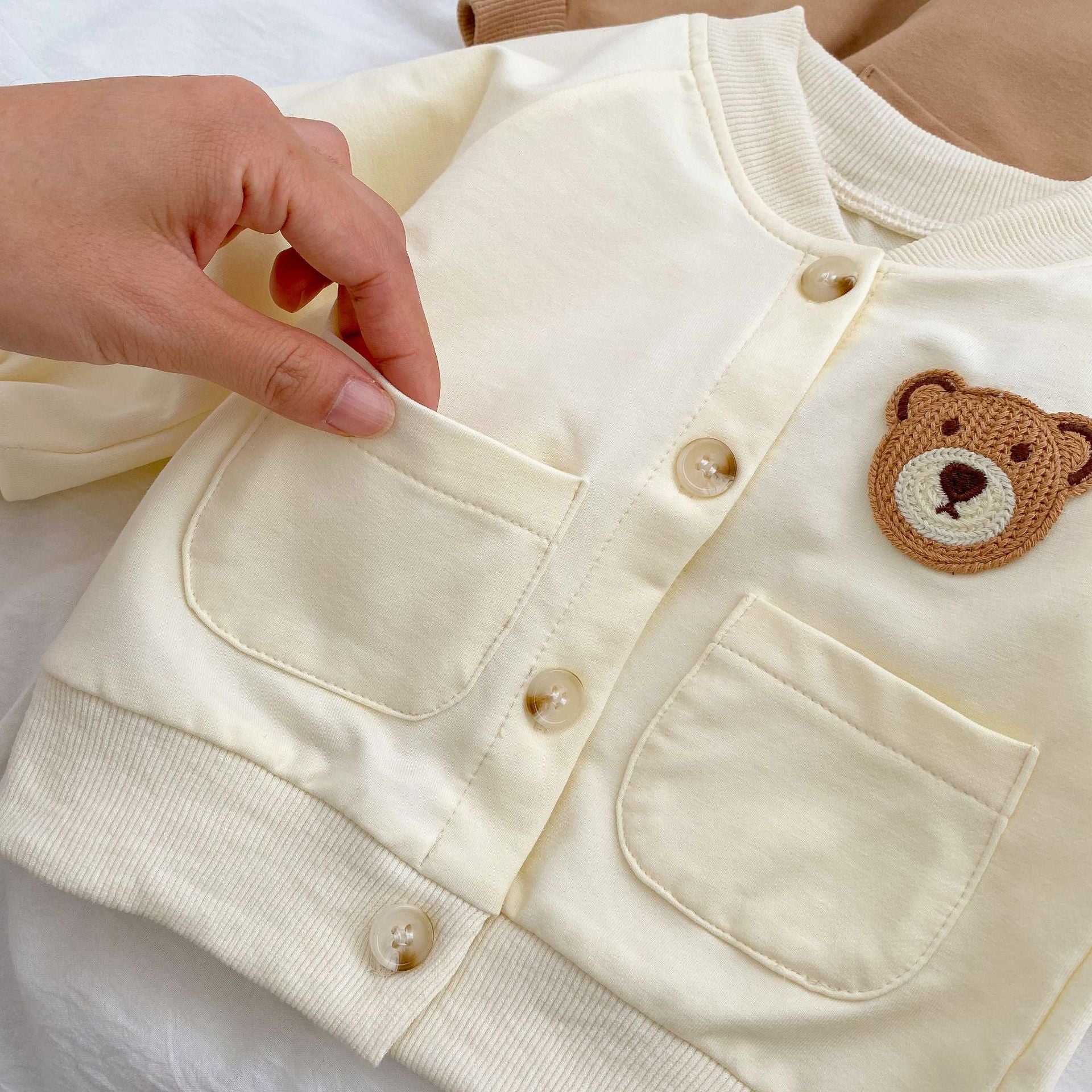 A cute baby wearing a cartoon bear patched romper and coat set in beige, showcasing its adorable design and premium cotton material.