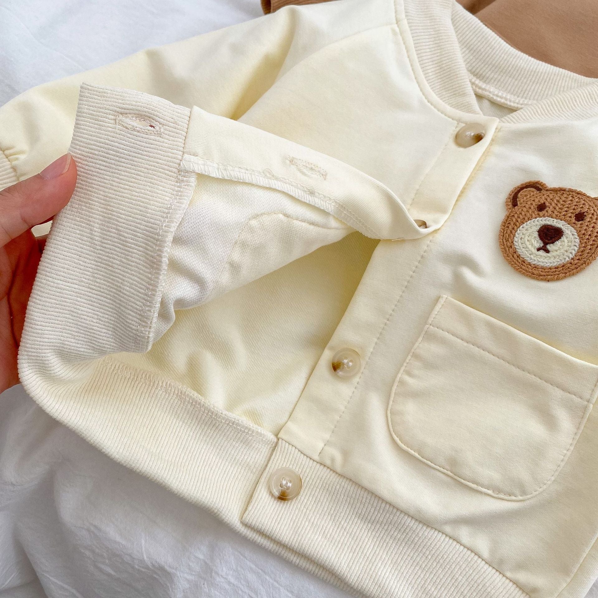 A cute baby wearing a cartoon bear patched romper and coat set in beige, showcasing its adorable design and premium cotton material.