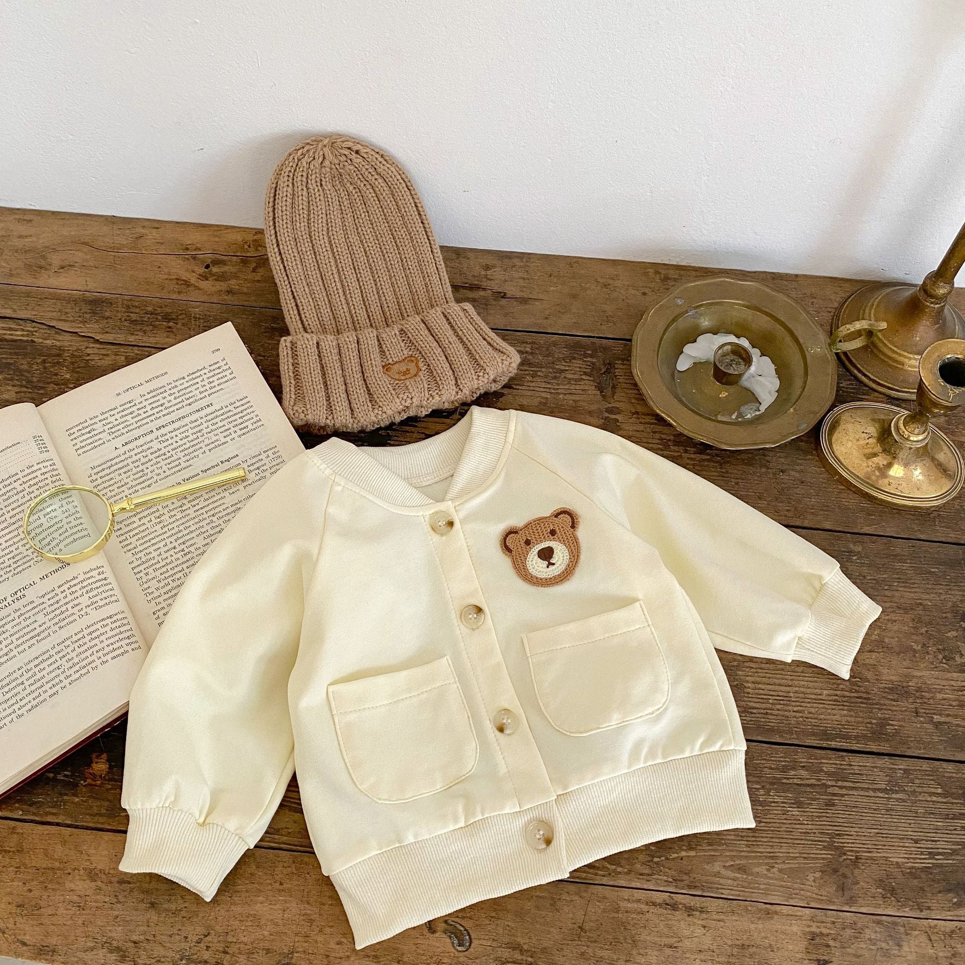 A cute baby wearing a cartoon bear patched romper and coat set in beige, showcasing its adorable design and premium cotton material.