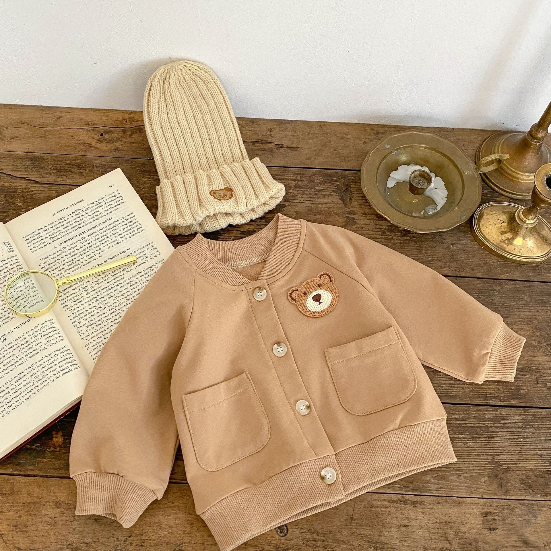 A cute baby wearing a cartoon bear patched romper and coat set in beige, showcasing its adorable design and premium cotton material.