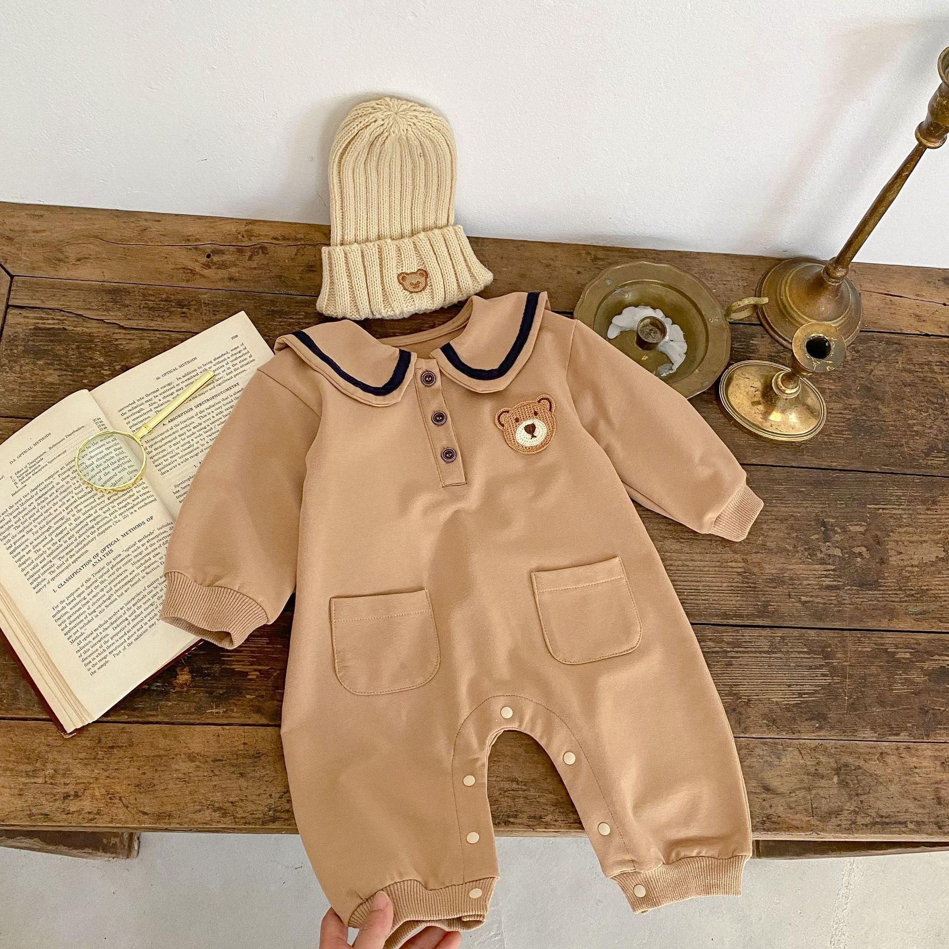 A cute baby wearing a cartoon bear patched romper and coat set in beige, showcasing its adorable design and premium cotton material.