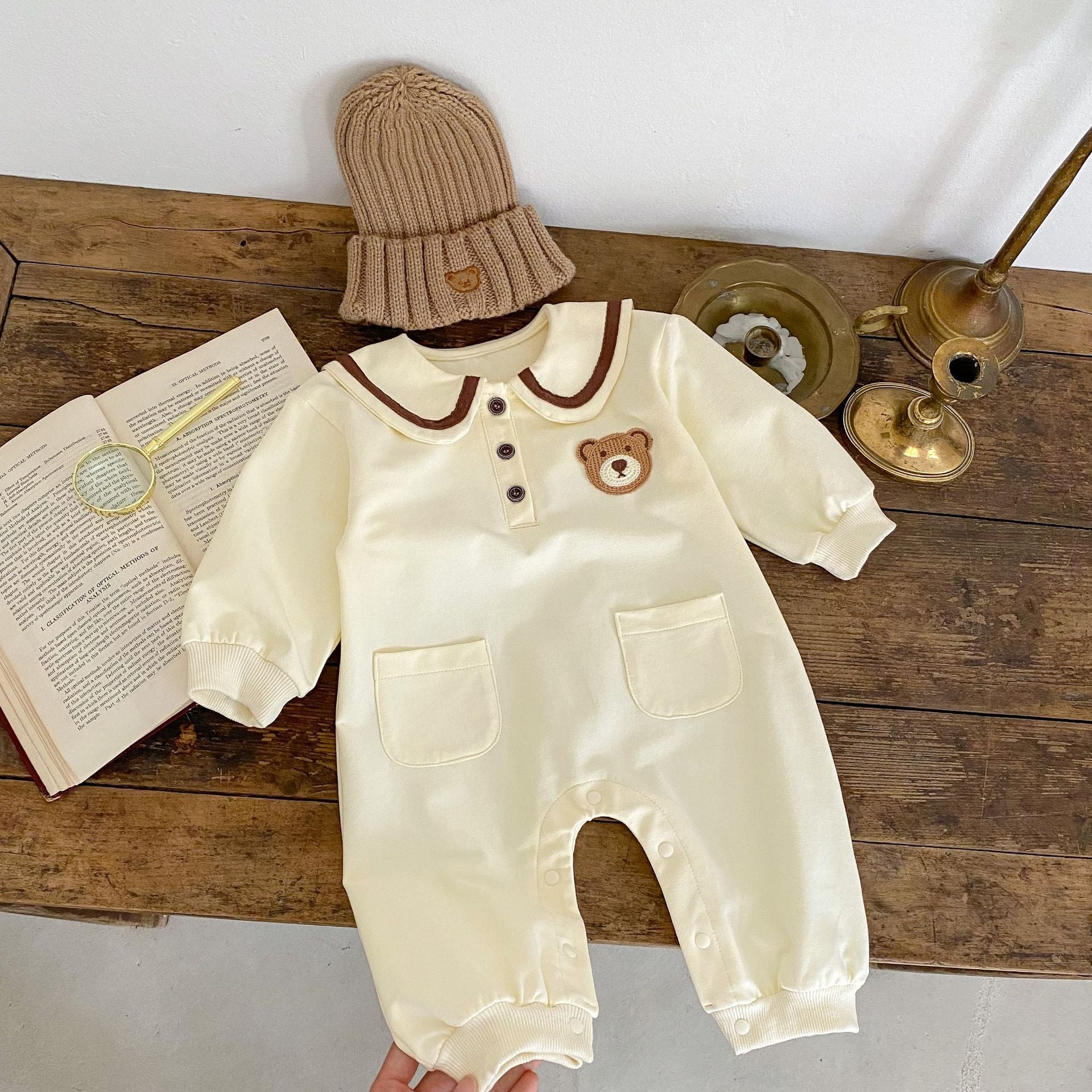 A cute baby wearing a cartoon bear patched romper and coat set in beige, showcasing its adorable design and premium cotton material.