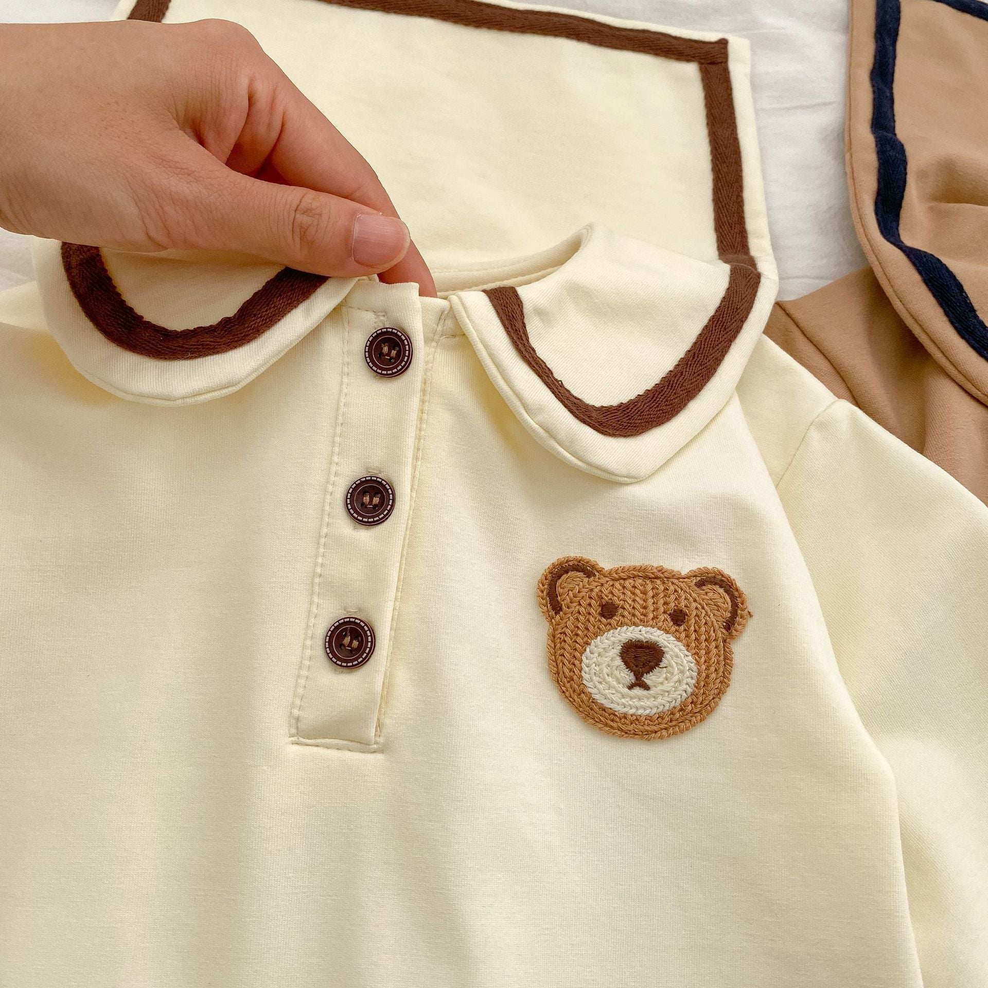 A cute baby wearing a cartoon bear patched romper and coat set in beige, showcasing its adorable design and premium cotton material.