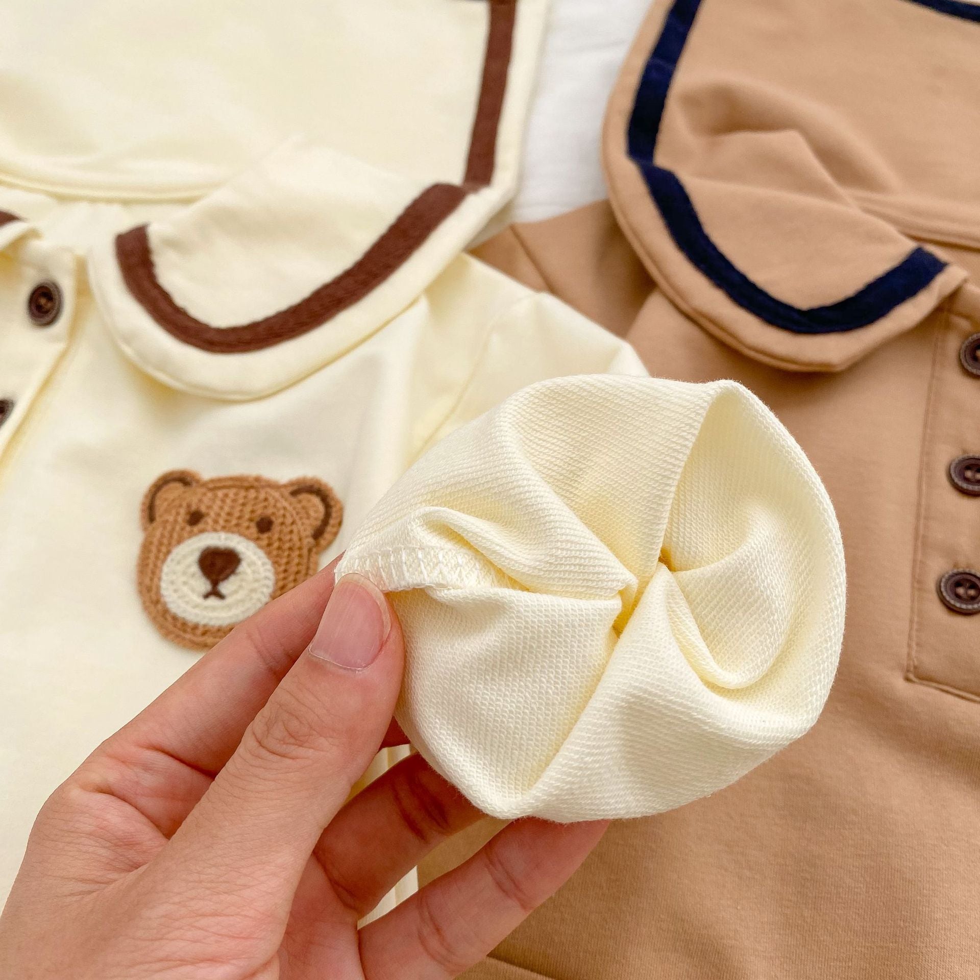 A cute baby wearing a cartoon bear patched romper and coat set in beige, showcasing its adorable design and premium cotton material.