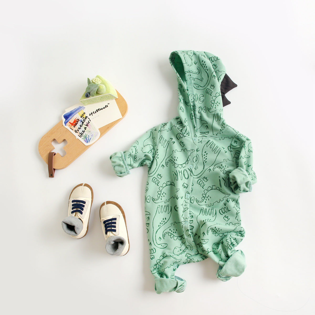 Baby wearing a cartoon dinosaur graphic romper with a matching hat, showcasing vibrant colors and snap button design.