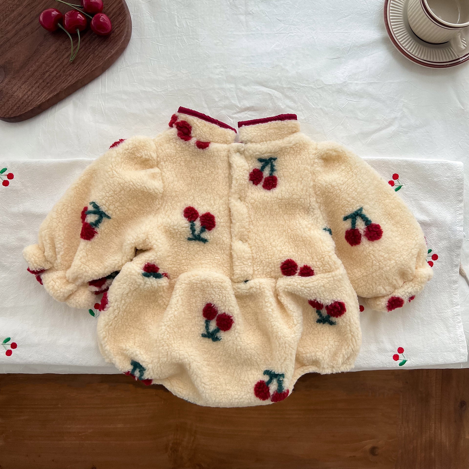 Baby girl wearing a thickened fleece onesie with a cherry pattern, in apricot color, perfect for spring and autumn.