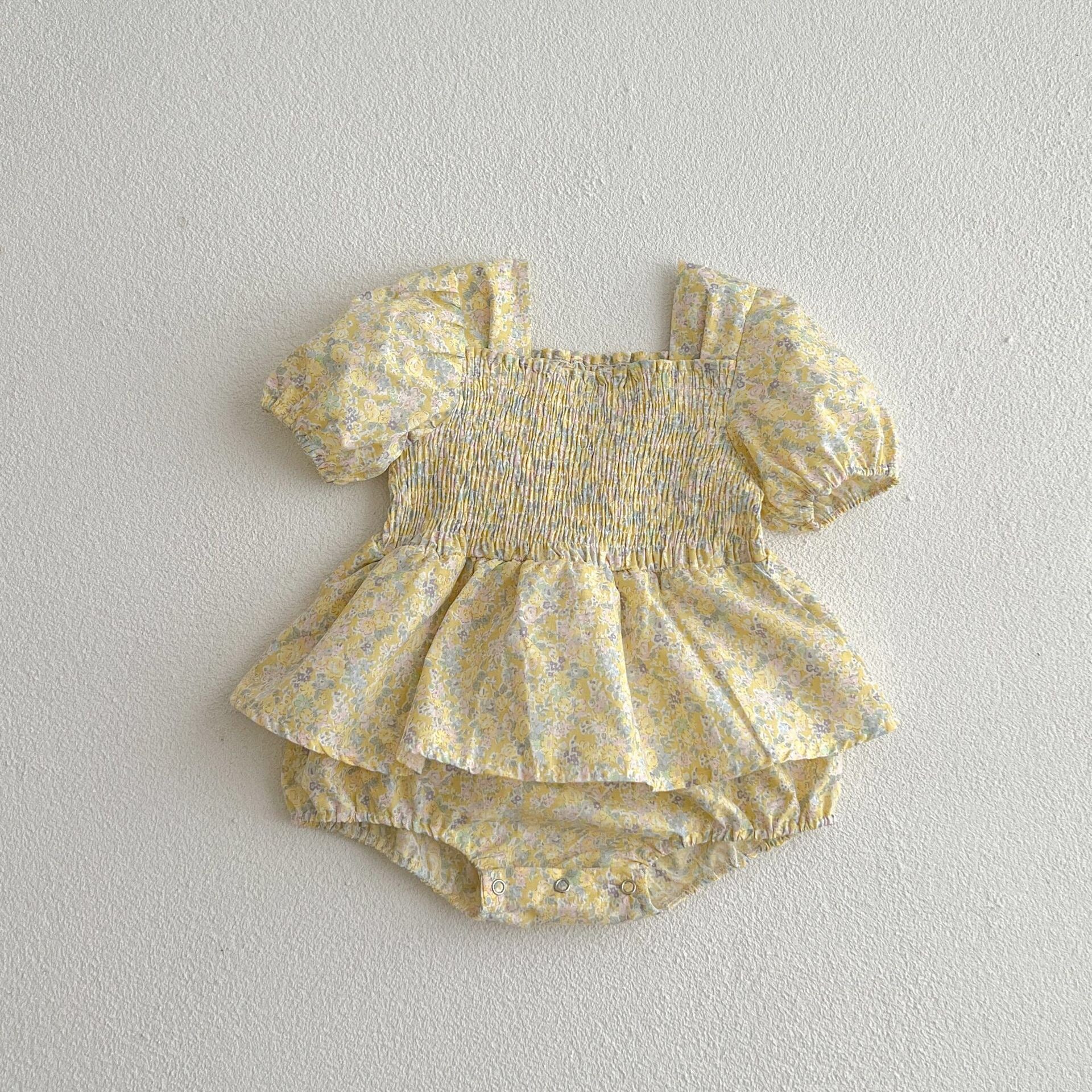 A cute baby girl wearing a yellow floral puff sleeve dress, perfect for summer outings.