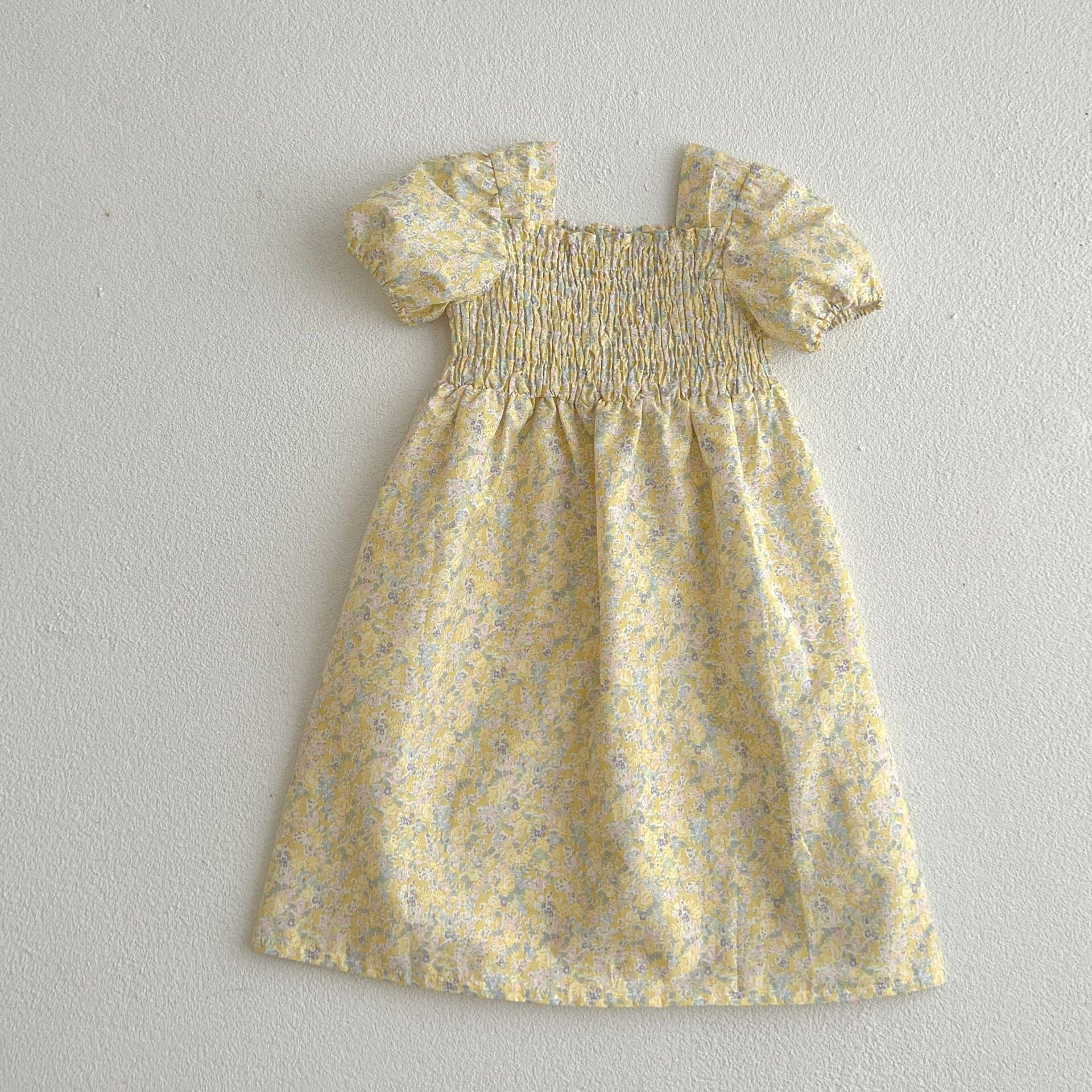 A cute baby girl wearing a yellow floral puff sleeve dress, perfect for summer outings.