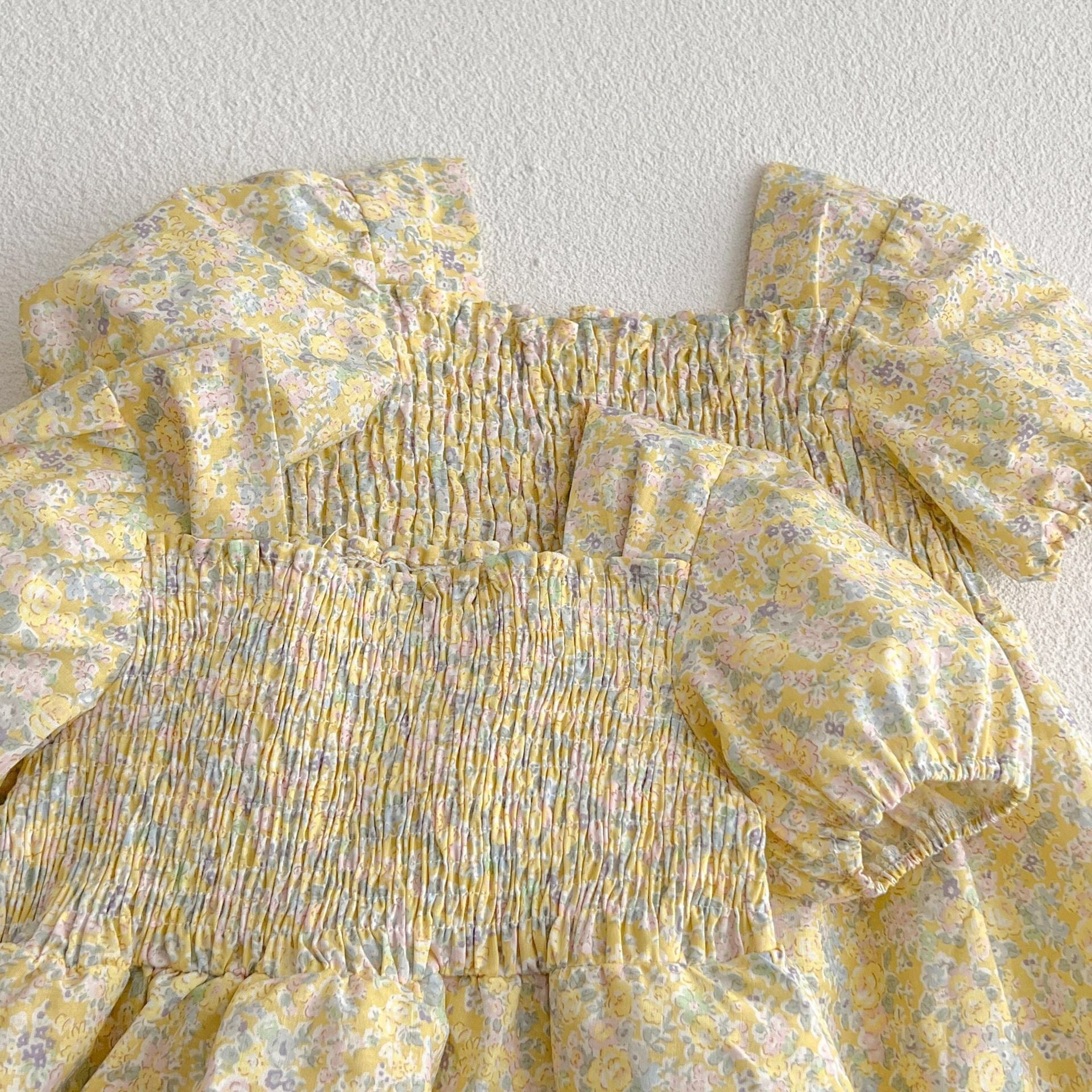 A cute baby girl wearing a yellow floral puff sleeve dress, perfect for summer outings.