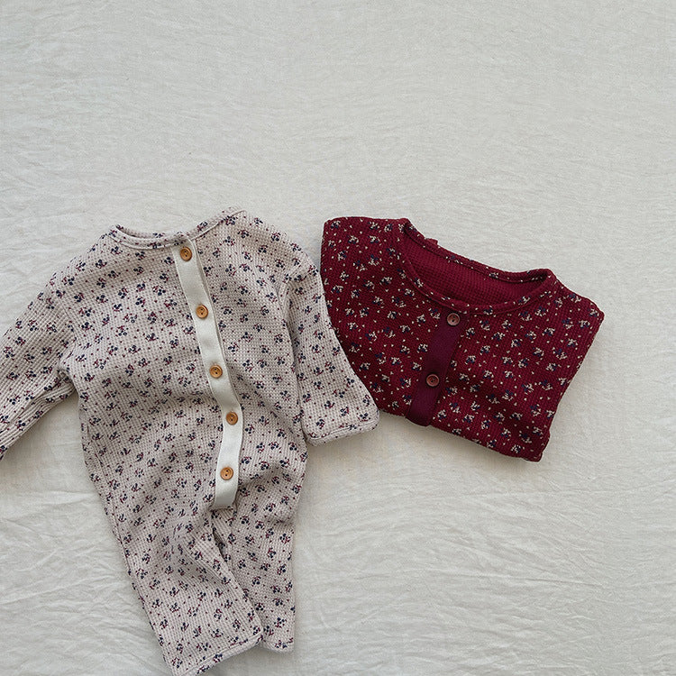 Baby girl wearing a floral patterned waffle knit romper with full button design in red and apricot colors.