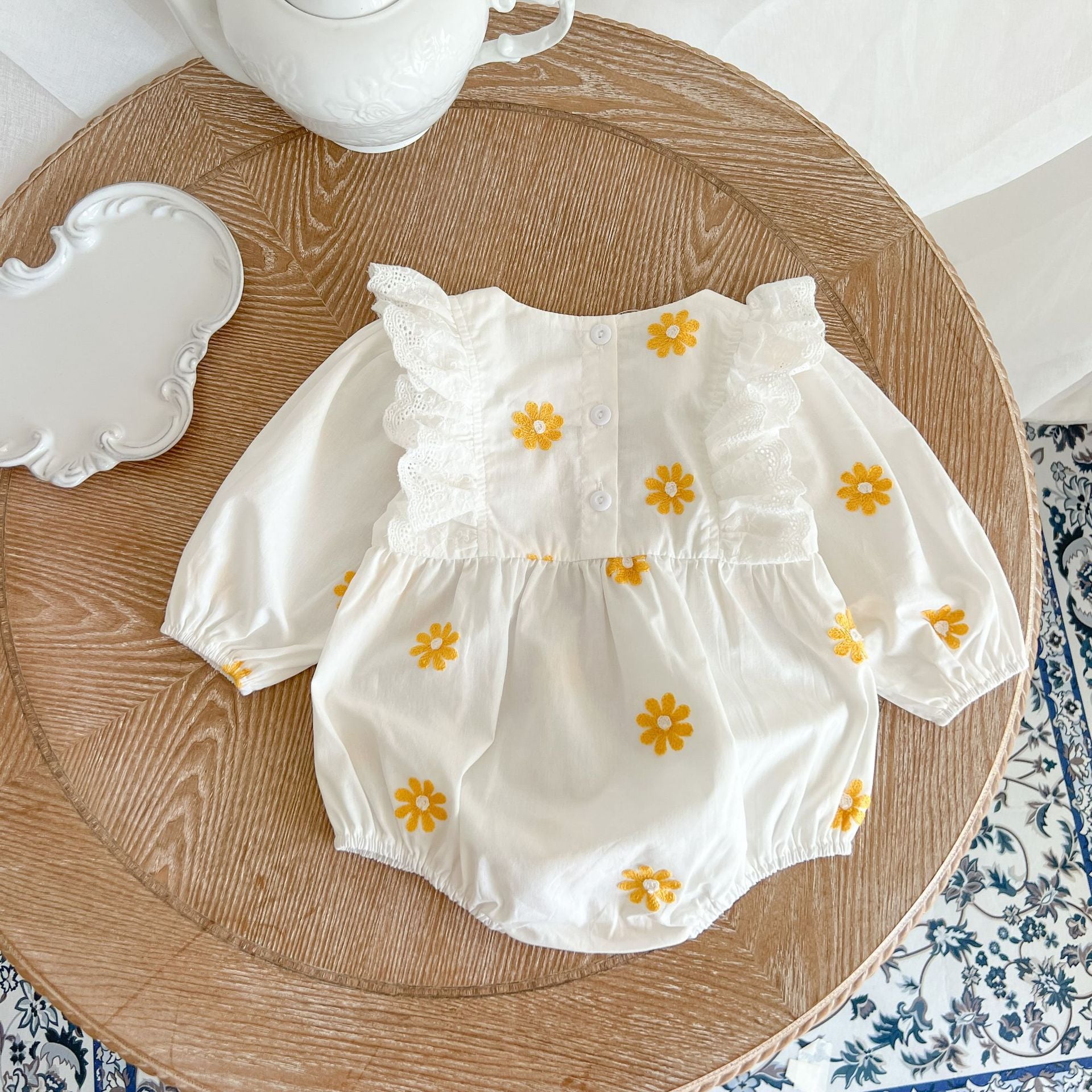 A baby girl wearing a floral embroidered onesie with ruffle design and square collar, showcasing a stylish and comfortable look.