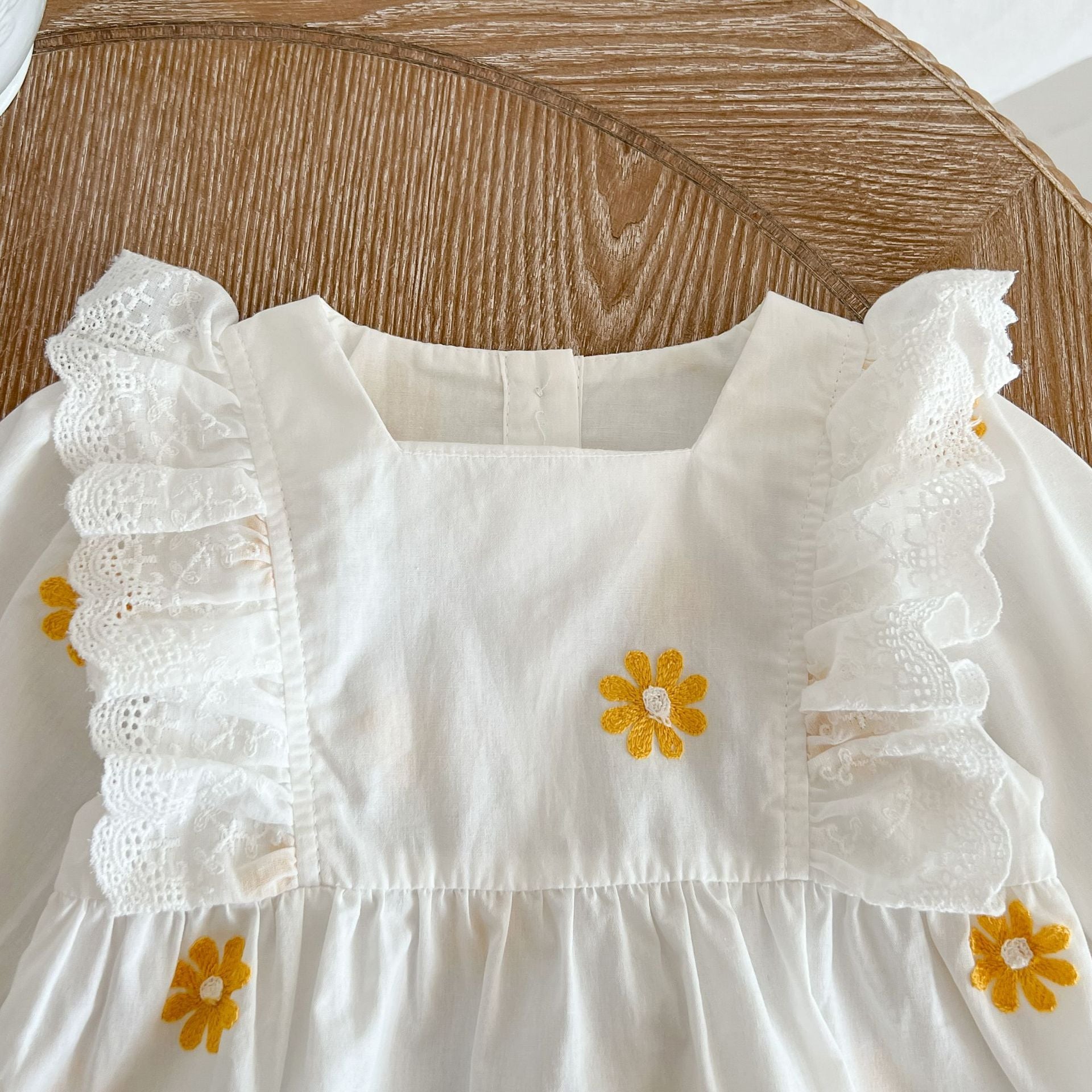 A baby girl wearing a floral embroidered onesie with ruffle design and square collar, showcasing a stylish and comfortable look.