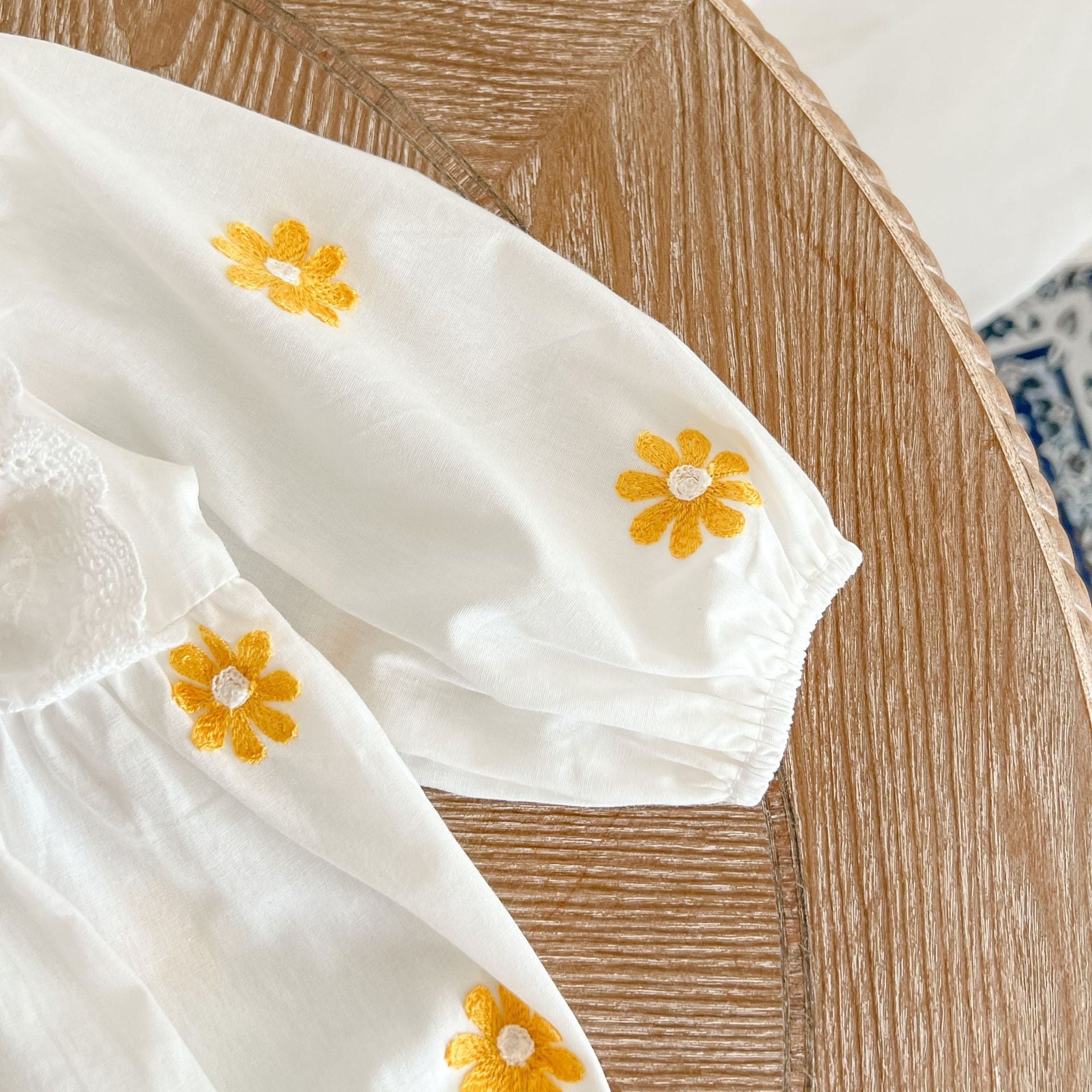 A baby girl wearing a floral embroidered onesie with ruffle design and square collar, showcasing a stylish and comfortable look.