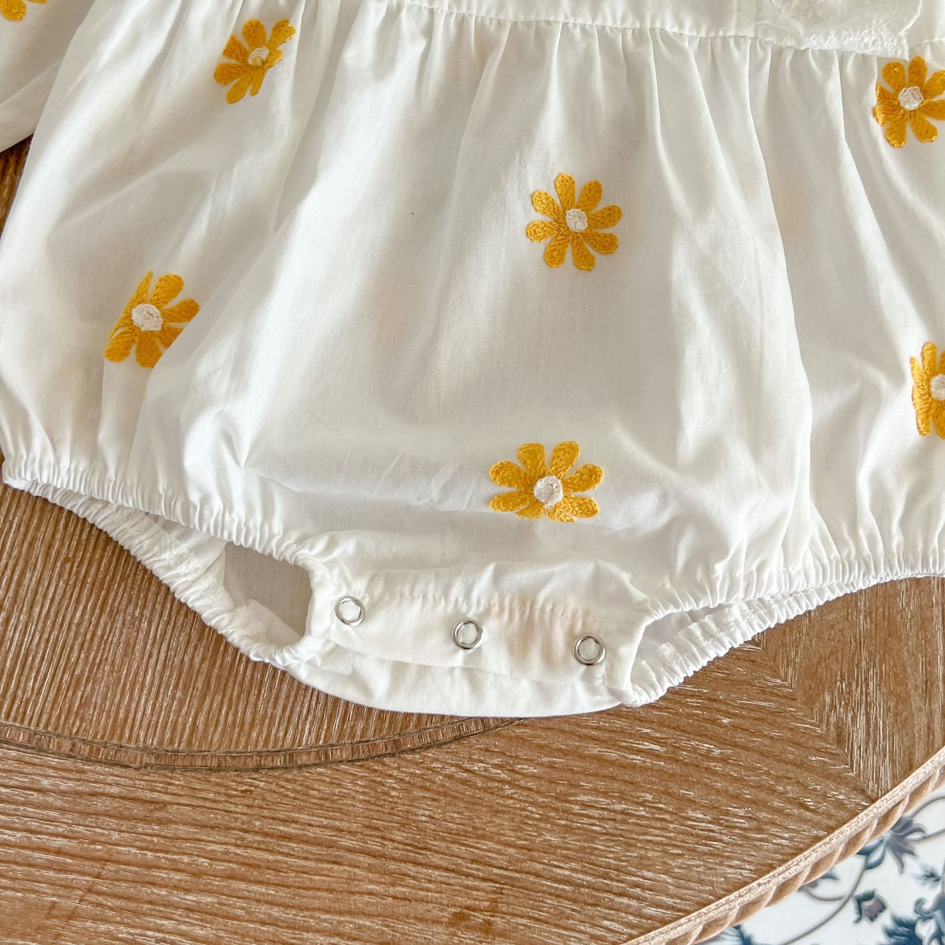 A baby girl wearing a floral embroidered onesie with ruffle design and square collar, showcasing a stylish and comfortable look.