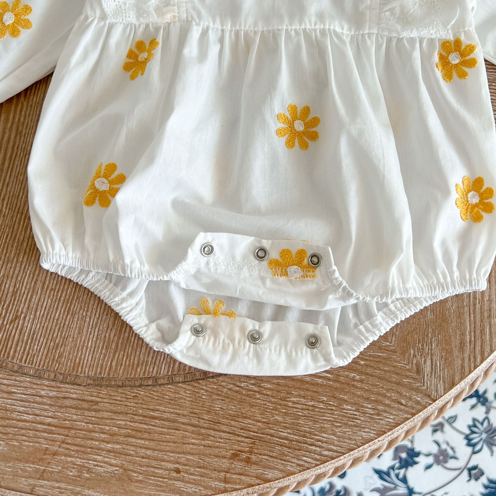 A baby girl wearing a floral embroidered onesie with ruffle design and square collar, showcasing a stylish and comfortable look.