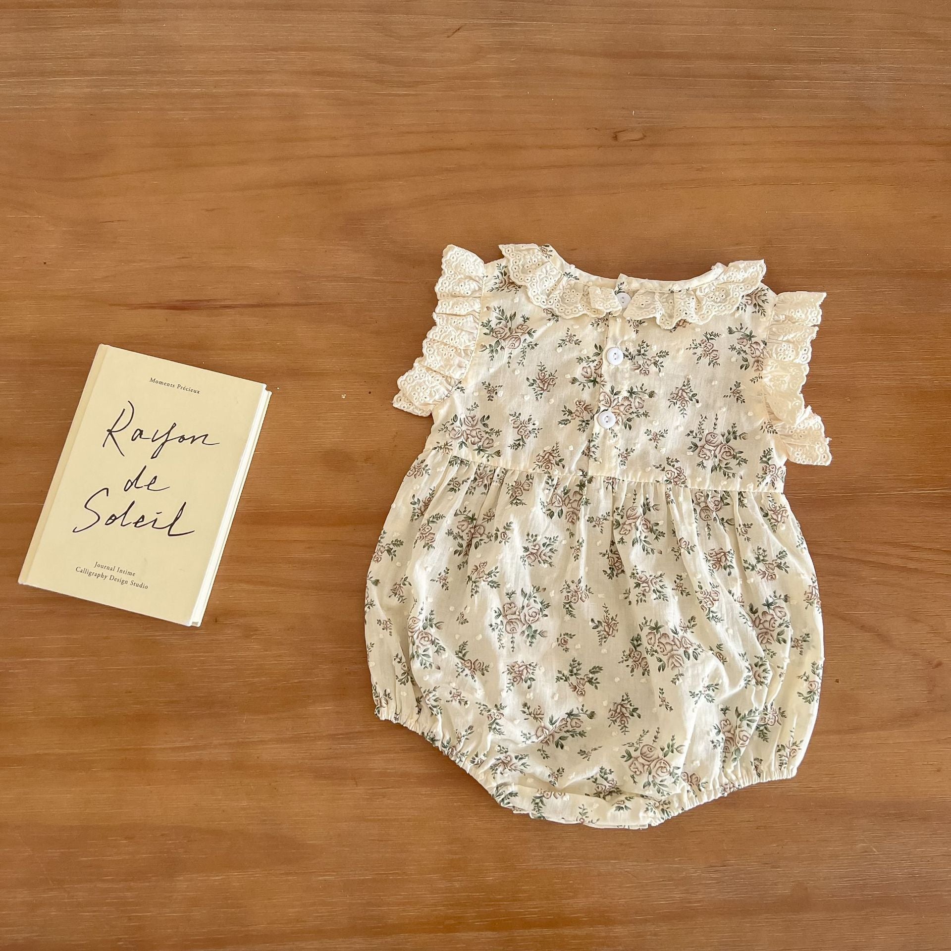 A beautiful baby girl wearing a floral print lace ruffle sleeveless onesie in apricot color, showcasing delicate ruffles and a charming design.