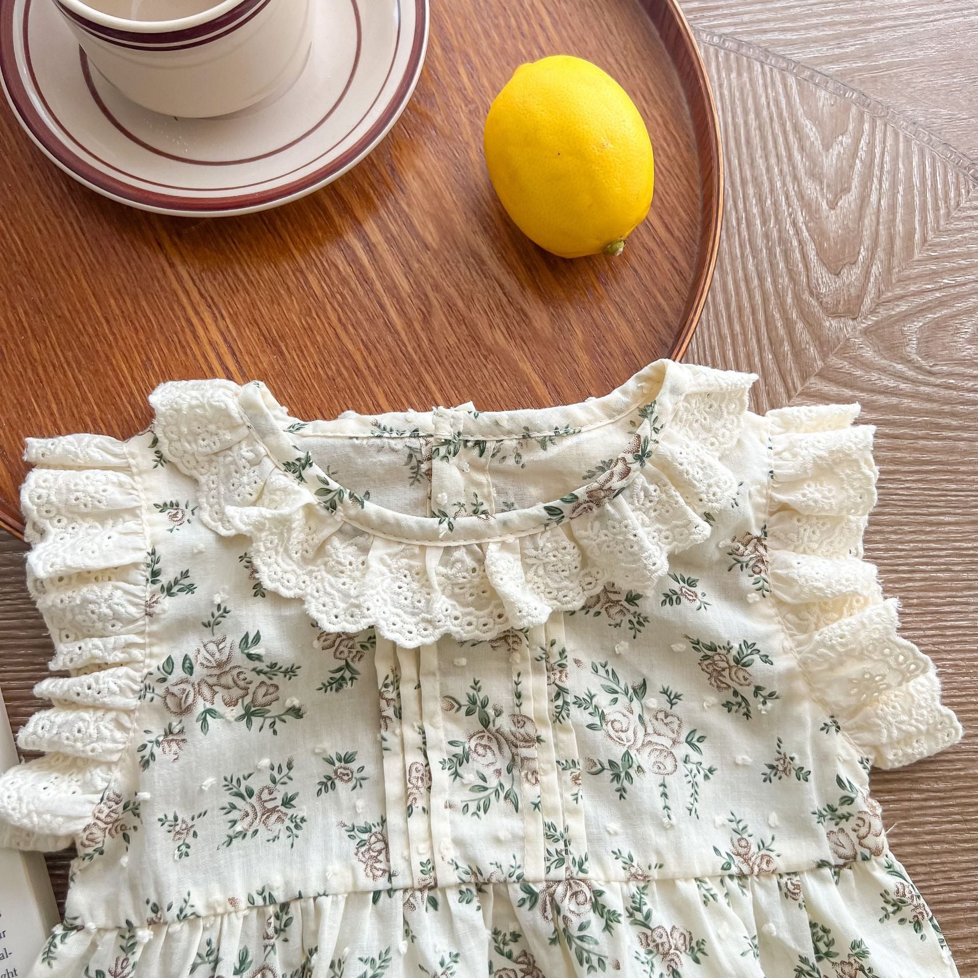 A beautiful baby girl wearing a floral print lace ruffle sleeveless onesie in apricot color, showcasing delicate ruffles and a charming design.