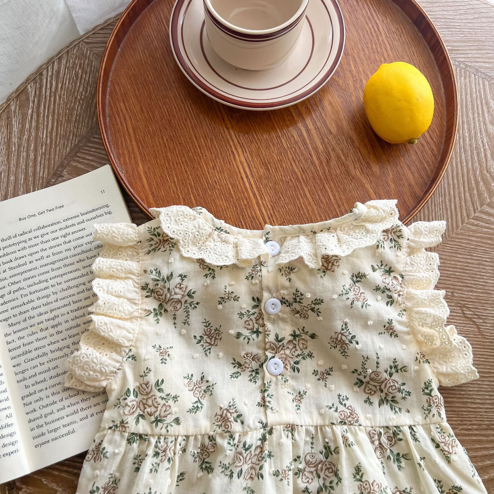 A beautiful baby girl wearing a floral print lace ruffle sleeveless onesie in apricot color, showcasing delicate ruffles and a charming design.