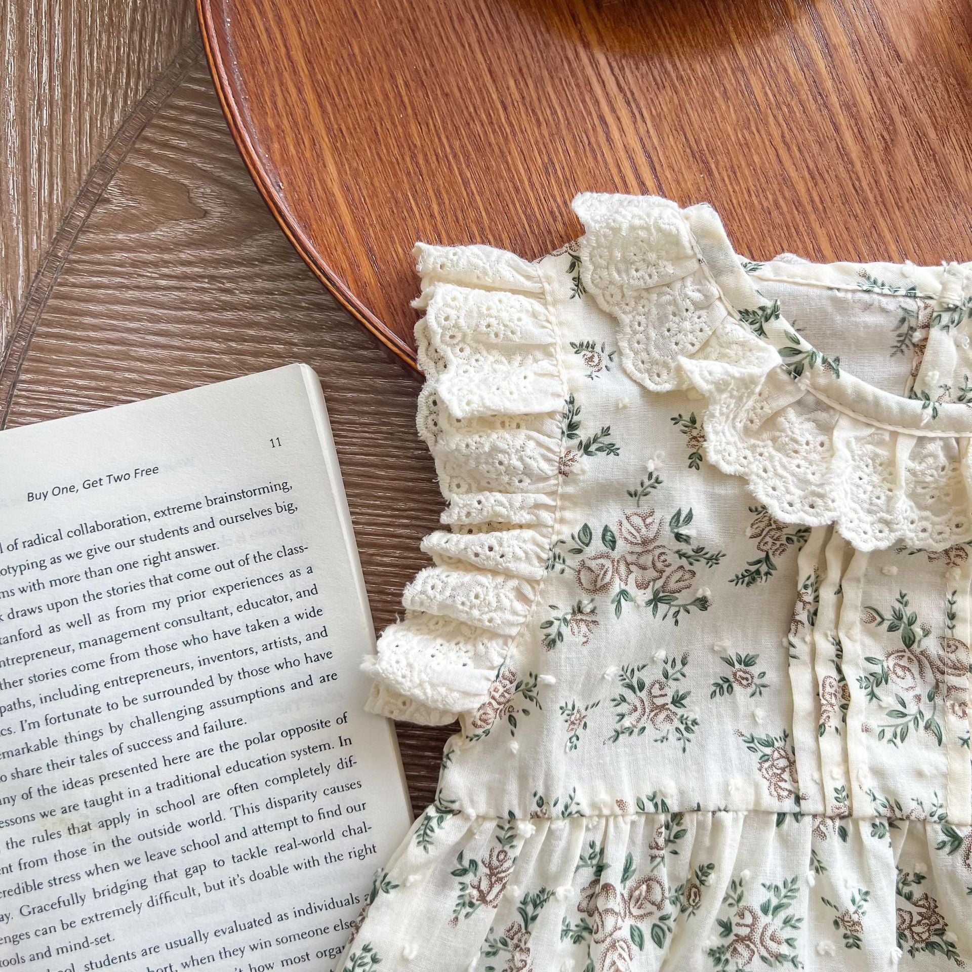 A beautiful baby girl wearing a floral print lace ruffle sleeveless onesie in apricot color, showcasing delicate ruffles and a charming design.