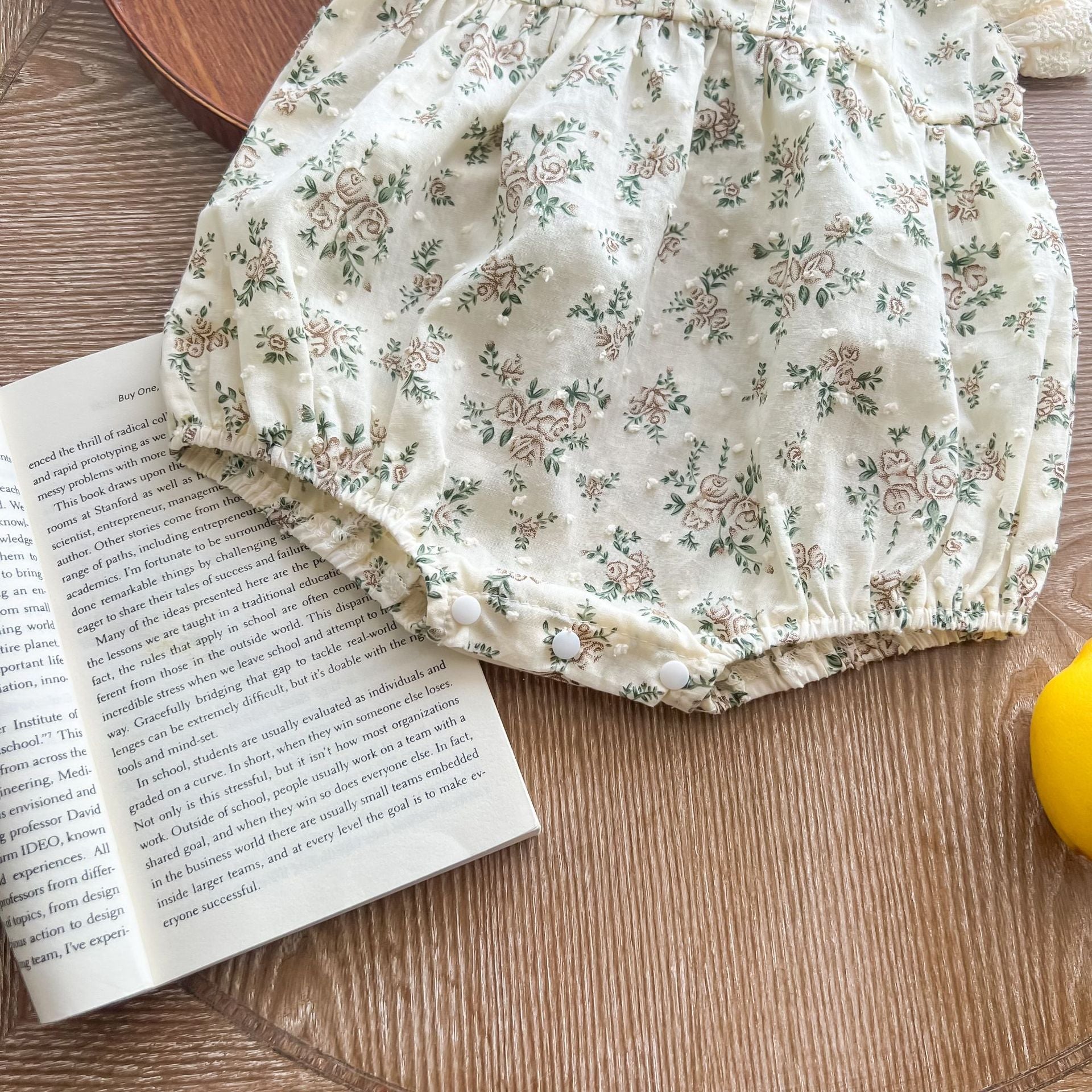 A beautiful baby girl wearing a floral print lace ruffle sleeveless onesie in apricot color, showcasing delicate ruffles and a charming design.