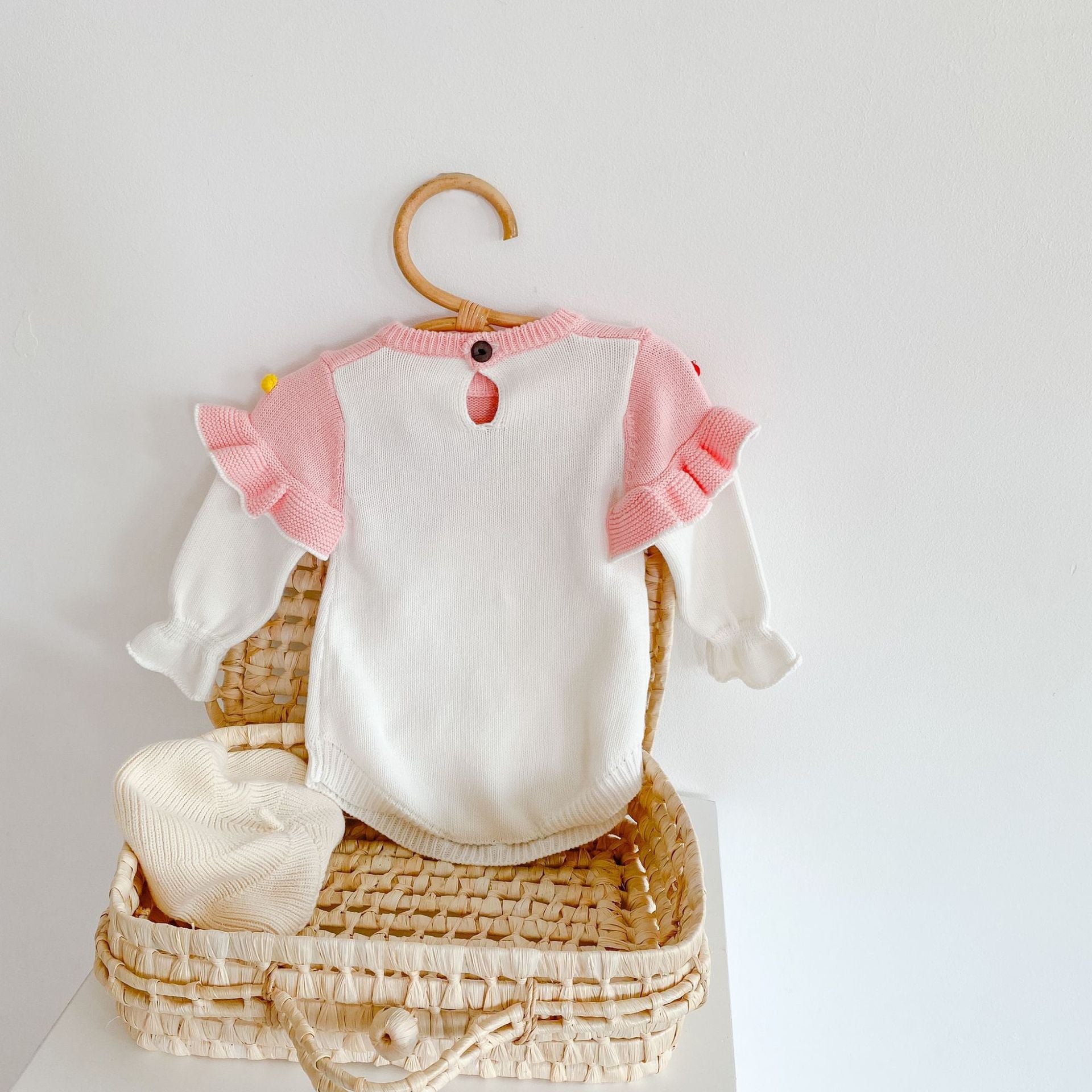 Colorful handmade knitted pullover for baby girl featuring ball patches and ruffle trim in pink.