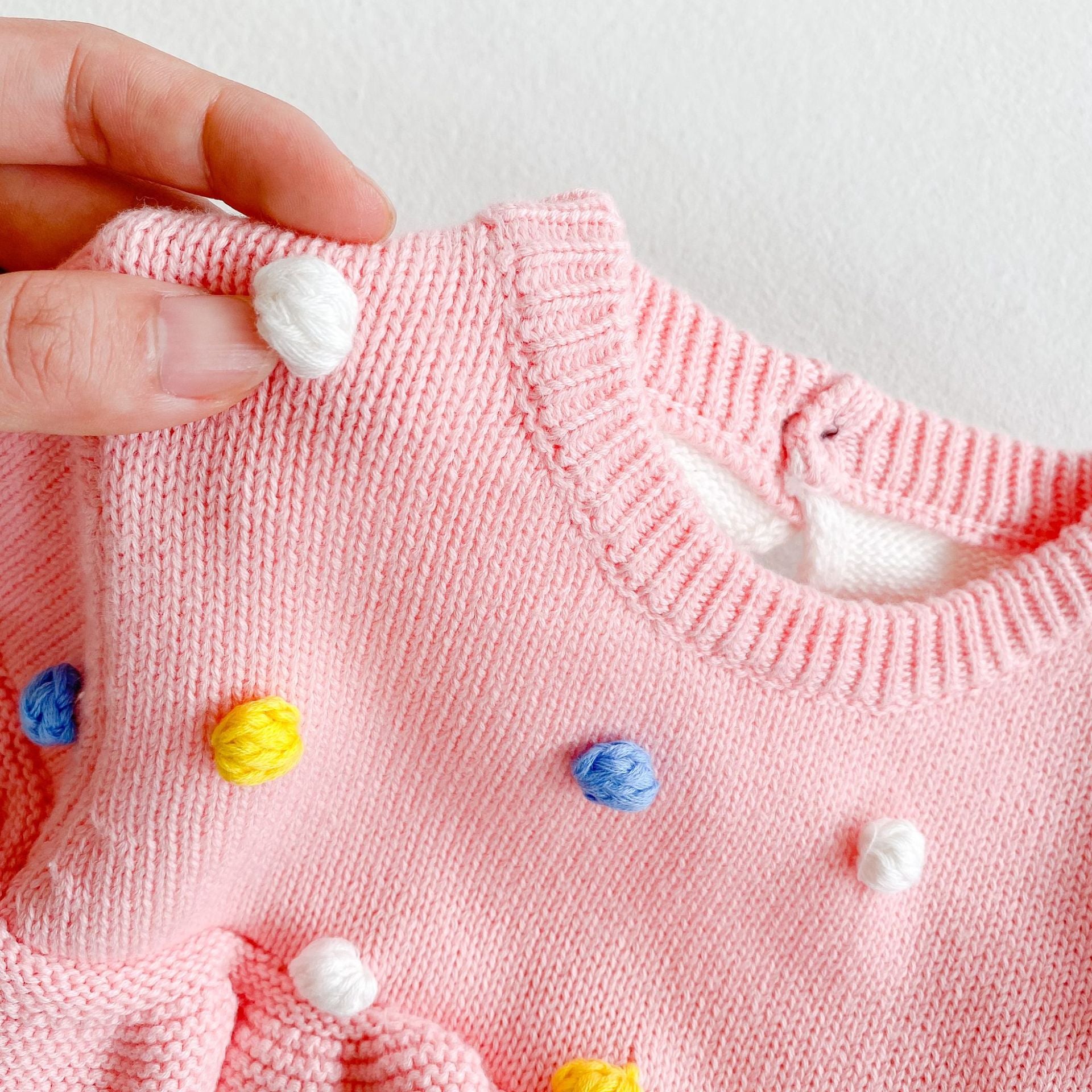 Colorful handmade knitted pullover for baby girl featuring ball patches and ruffle trim in pink.