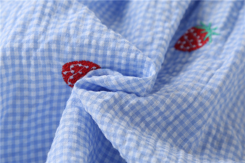 Adorable baby girl wearing a plaid jumpsuit with strawberry embroidery and snap button closure, showcasing a playful summer outfit.