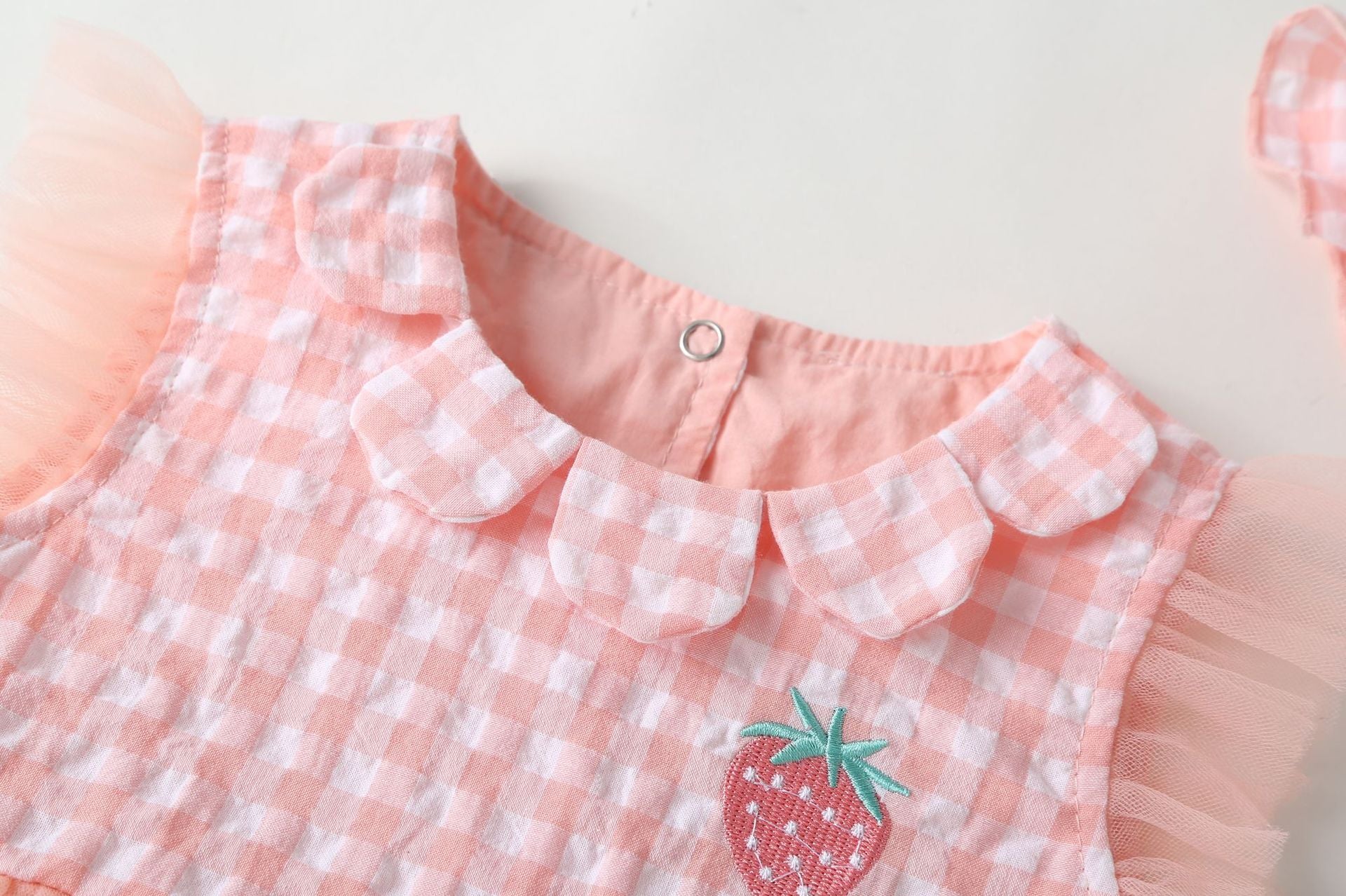 Baby girl dress featuring plaid graphic design, strawberry embroidery, and mesh overlay in pink and green colors.