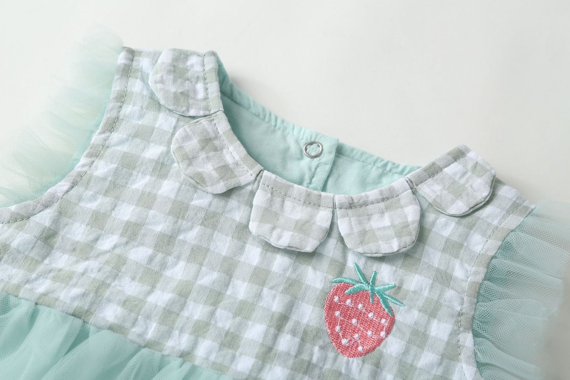 Baby girl dress featuring plaid graphic design, strawberry embroidery, and mesh overlay in pink and green colors.