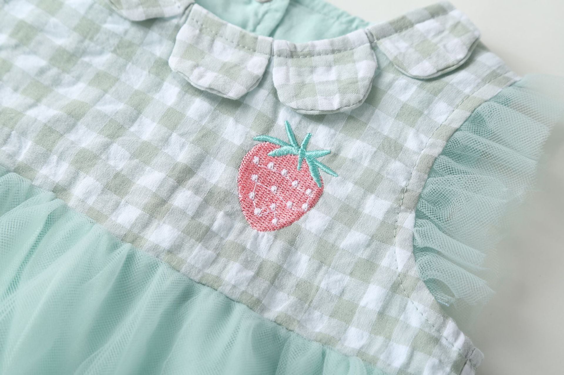 Baby girl dress featuring plaid graphic design, strawberry embroidery, and mesh overlay in pink and green colors.