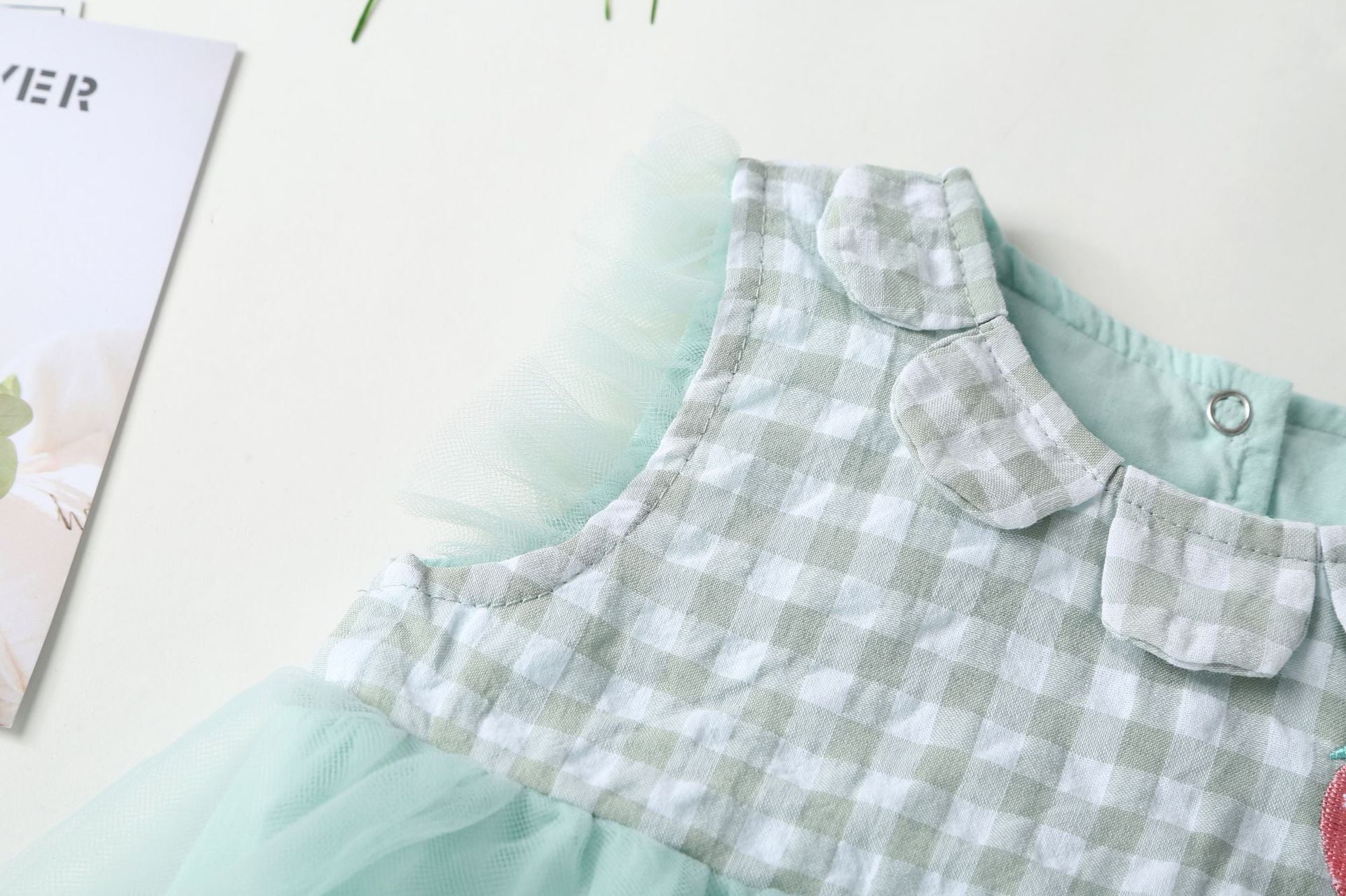 Baby girl dress featuring plaid graphic design, strawberry embroidery, and mesh overlay in pink and green colors.