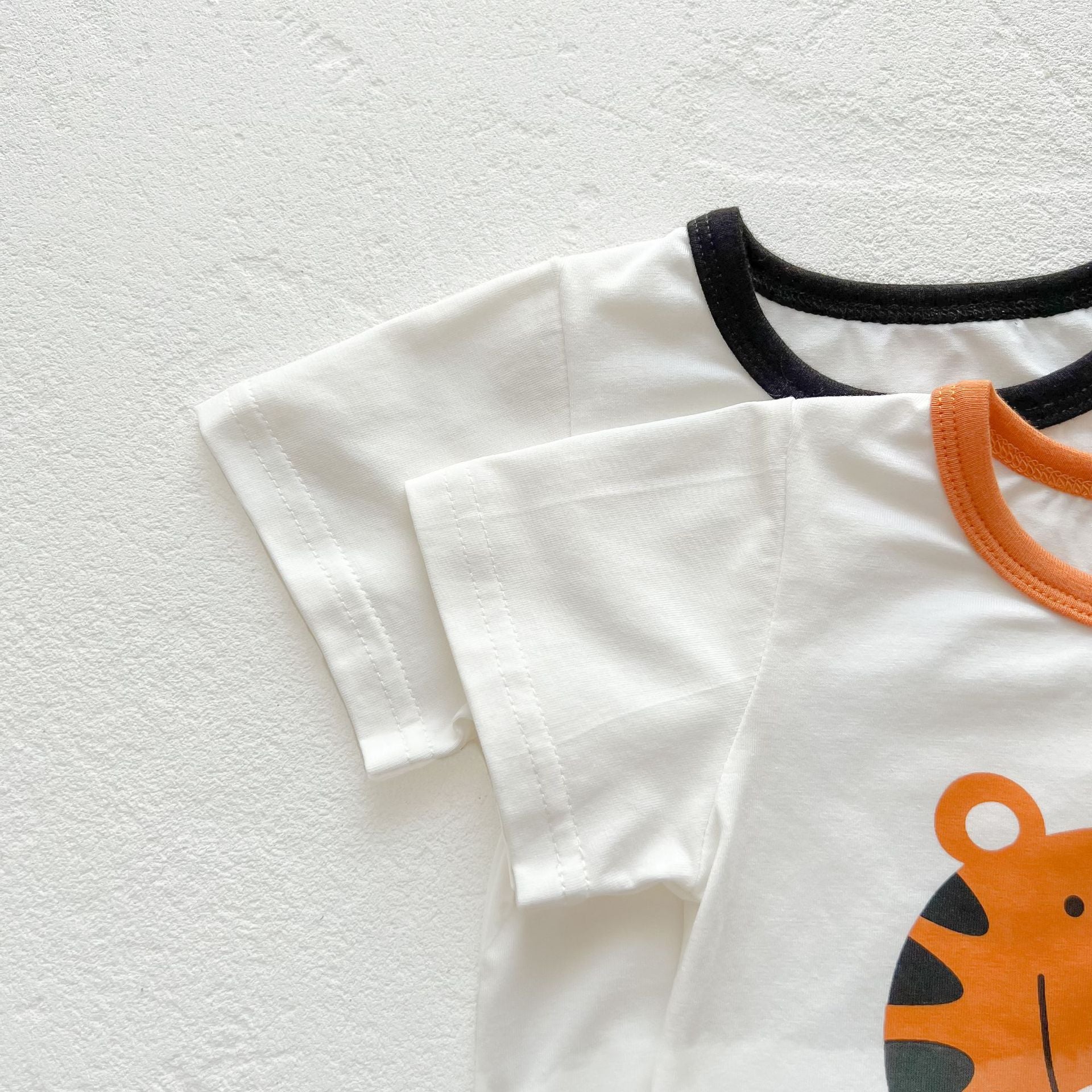 Baby girl onesie featuring a cartoon animal print with a round collar and short sleeves, available in white and orange colors.