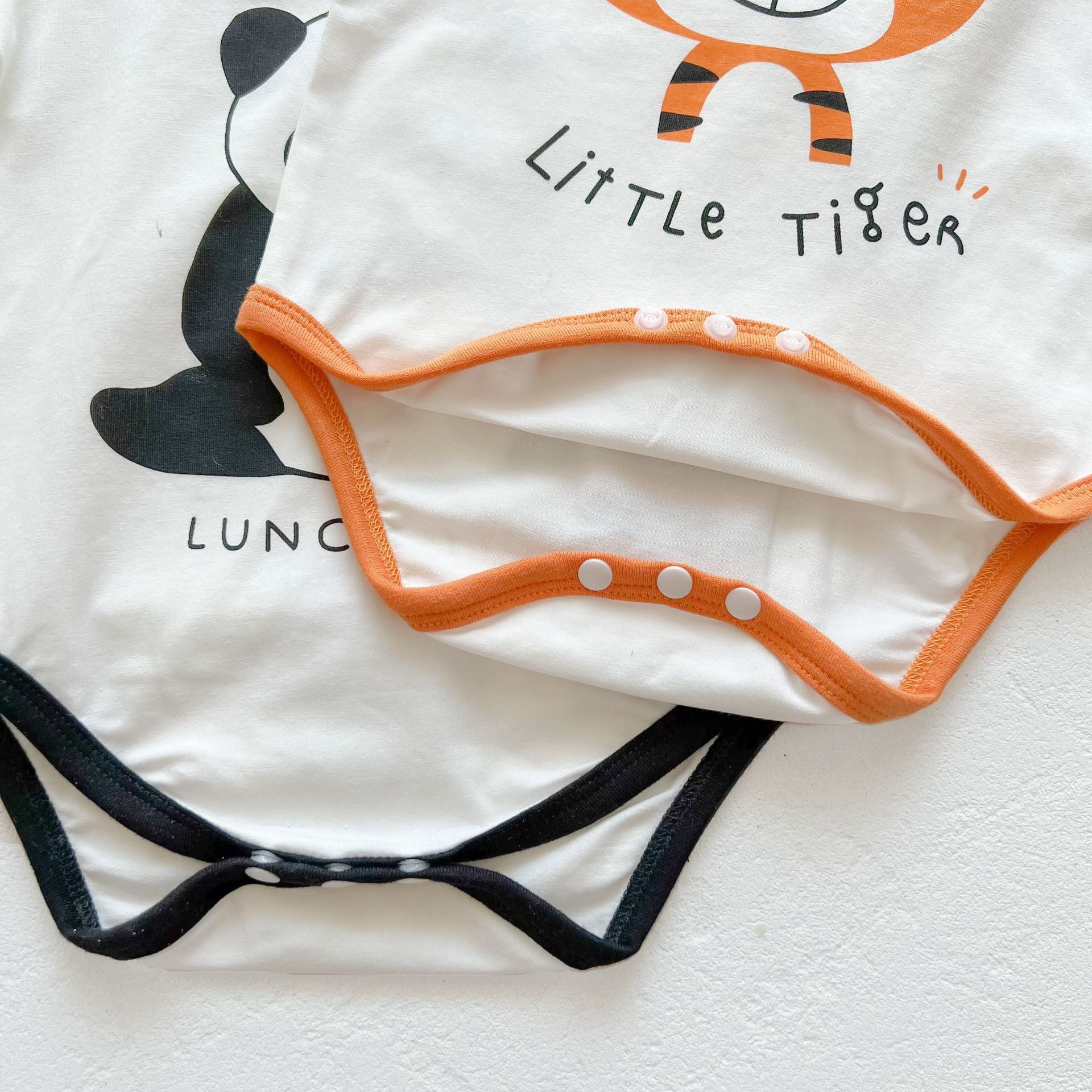 Baby girl onesie featuring a cartoon animal print with a round collar and short sleeves, available in white and orange colors.