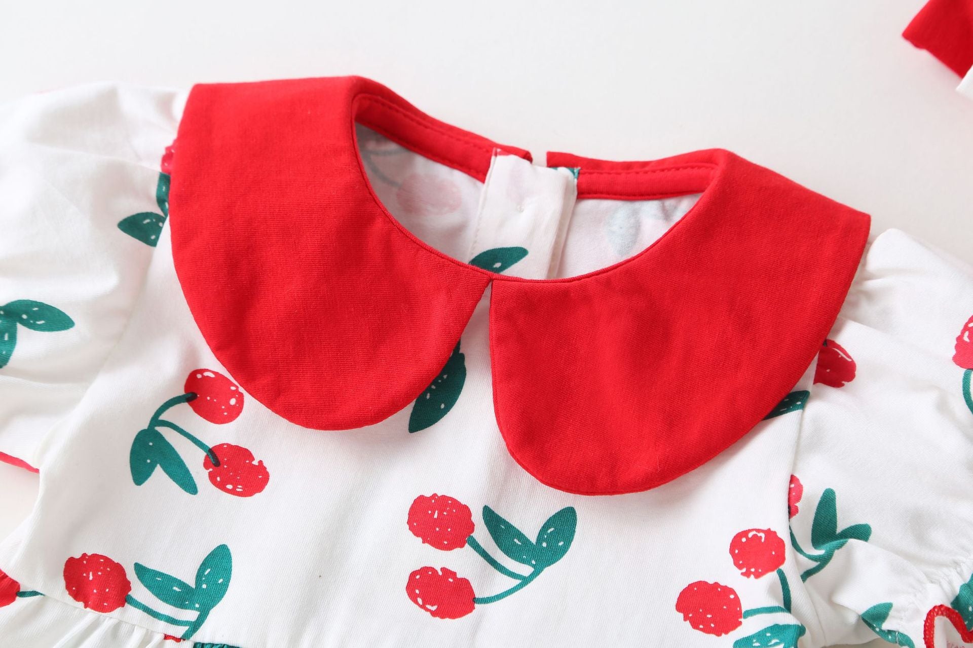 Adorable baby girl wearing a cherry print onesie with a round collar and short sleeves, perfect for summer outings.