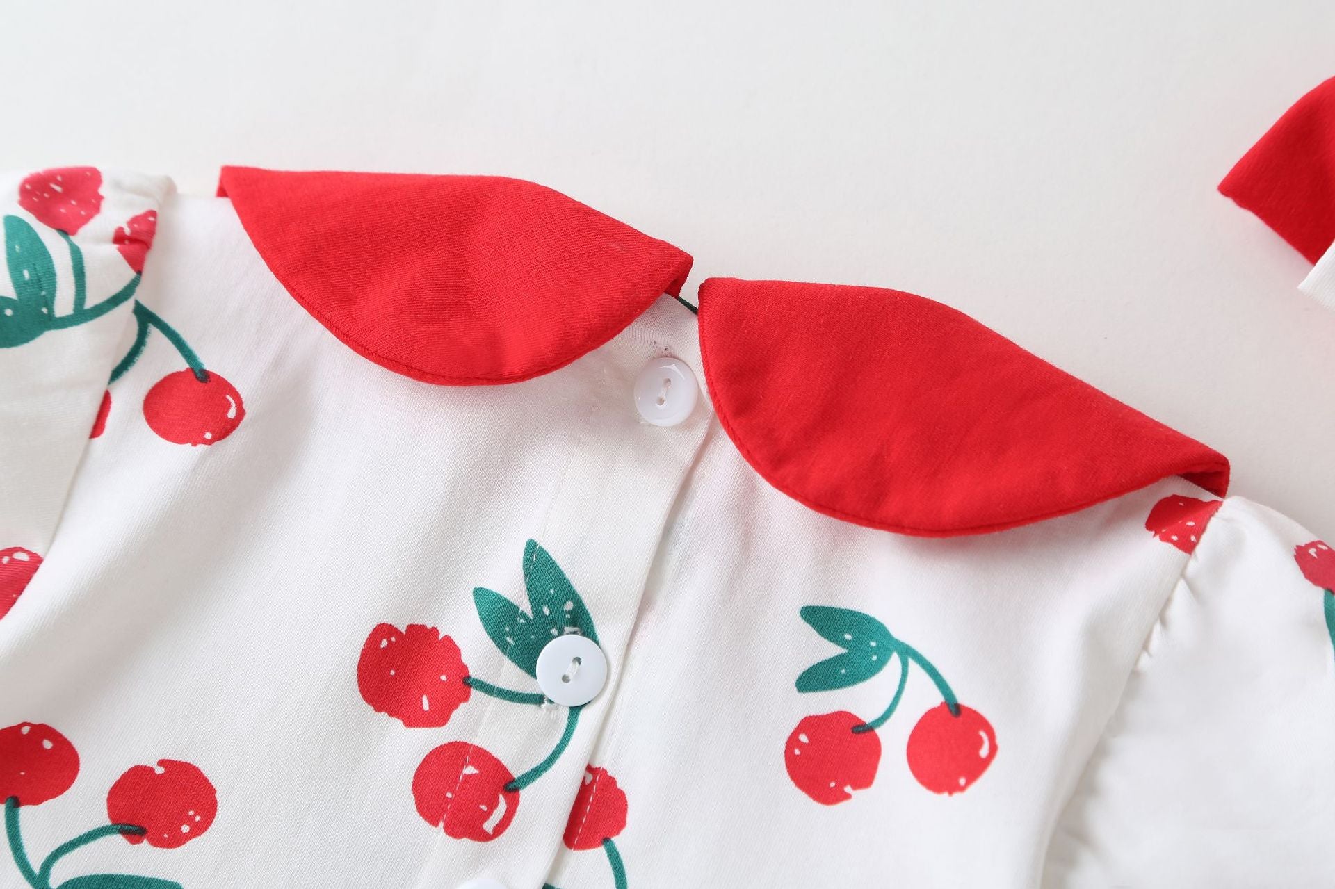 Adorable baby girl wearing a cherry print onesie with a round collar and short sleeves, perfect for summer outings.