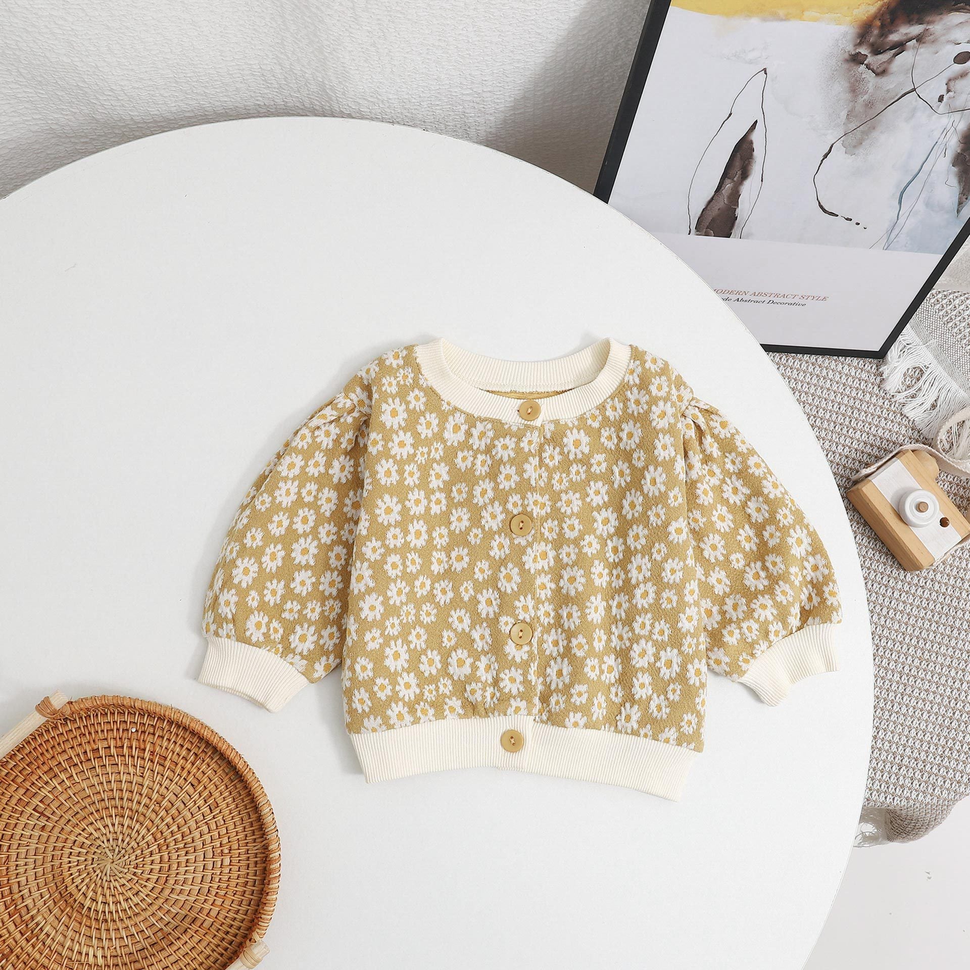 Baby girl cardigan featuring a daisy pattern and puff sleeves, available in black and yellow colors.