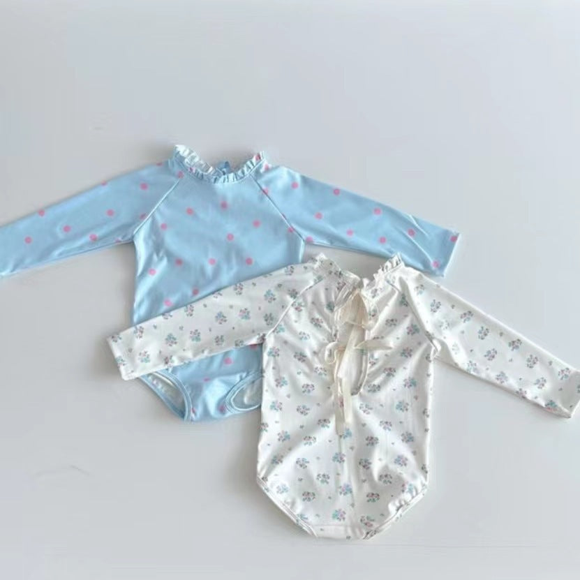 Baby girl wearing a long sleeve onesie with a ditsy flower pattern and a matching hat, showcasing the white and blue color options.