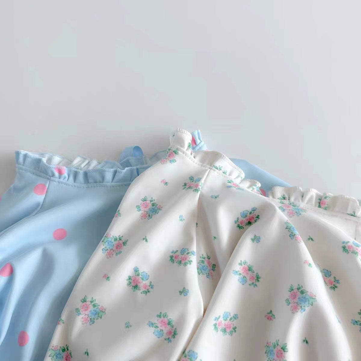 Baby girl wearing a long sleeve onesie with a ditsy flower pattern and a matching hat, showcasing the white and blue color options.