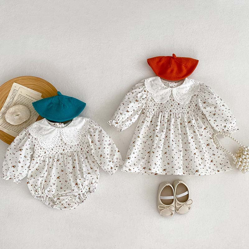 Baby girl wearing a floral pattern doll neck onesie and dress in white and beige, showcasing a cute and stylish design.