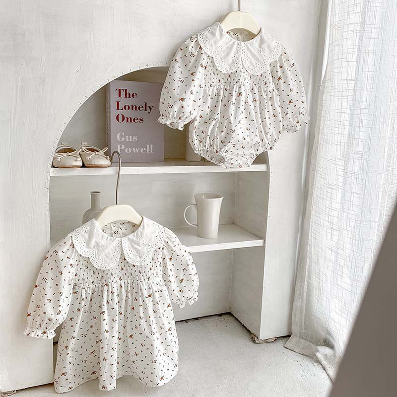 Baby girl wearing a floral pattern doll neck onesie and dress in white and beige, showcasing a cute and stylish design.