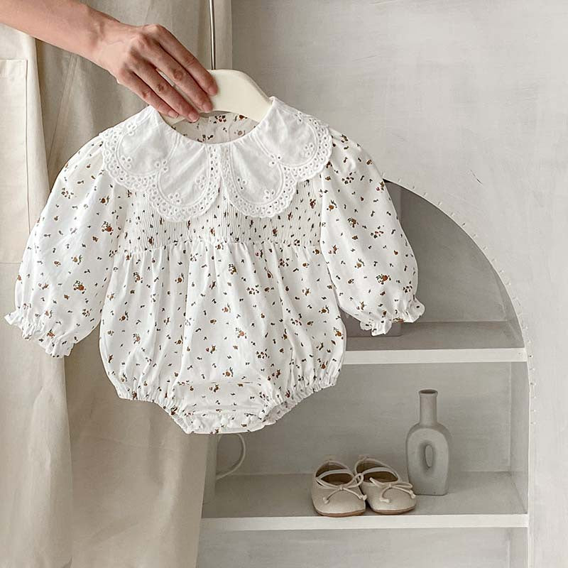 Baby girl wearing a floral pattern doll neck onesie and dress in white and beige, showcasing a cute and stylish design.